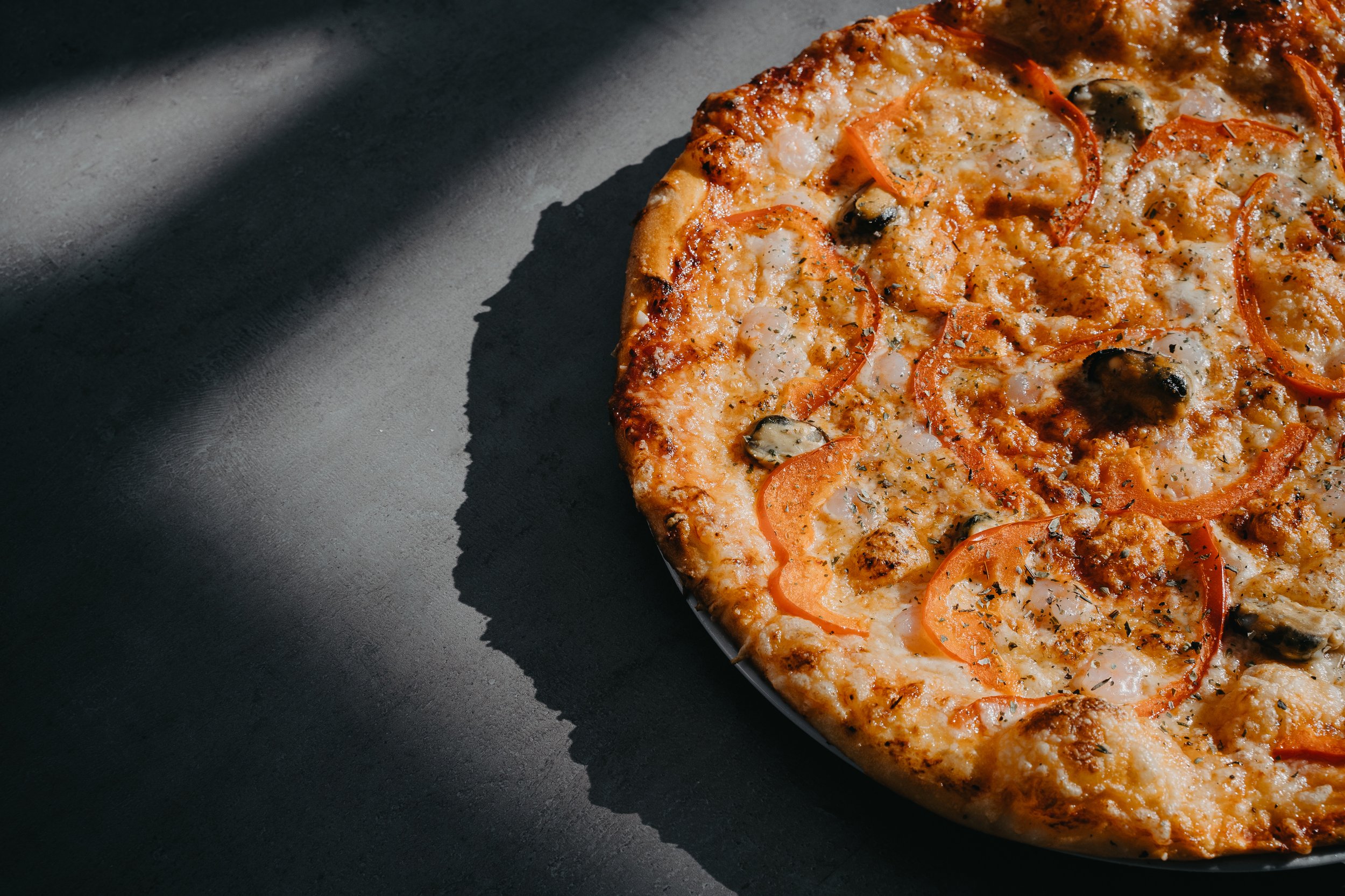 Close-up of a freshly baked pizza with cheese, red bell peppers, black olives, and sausage on a dark surface.