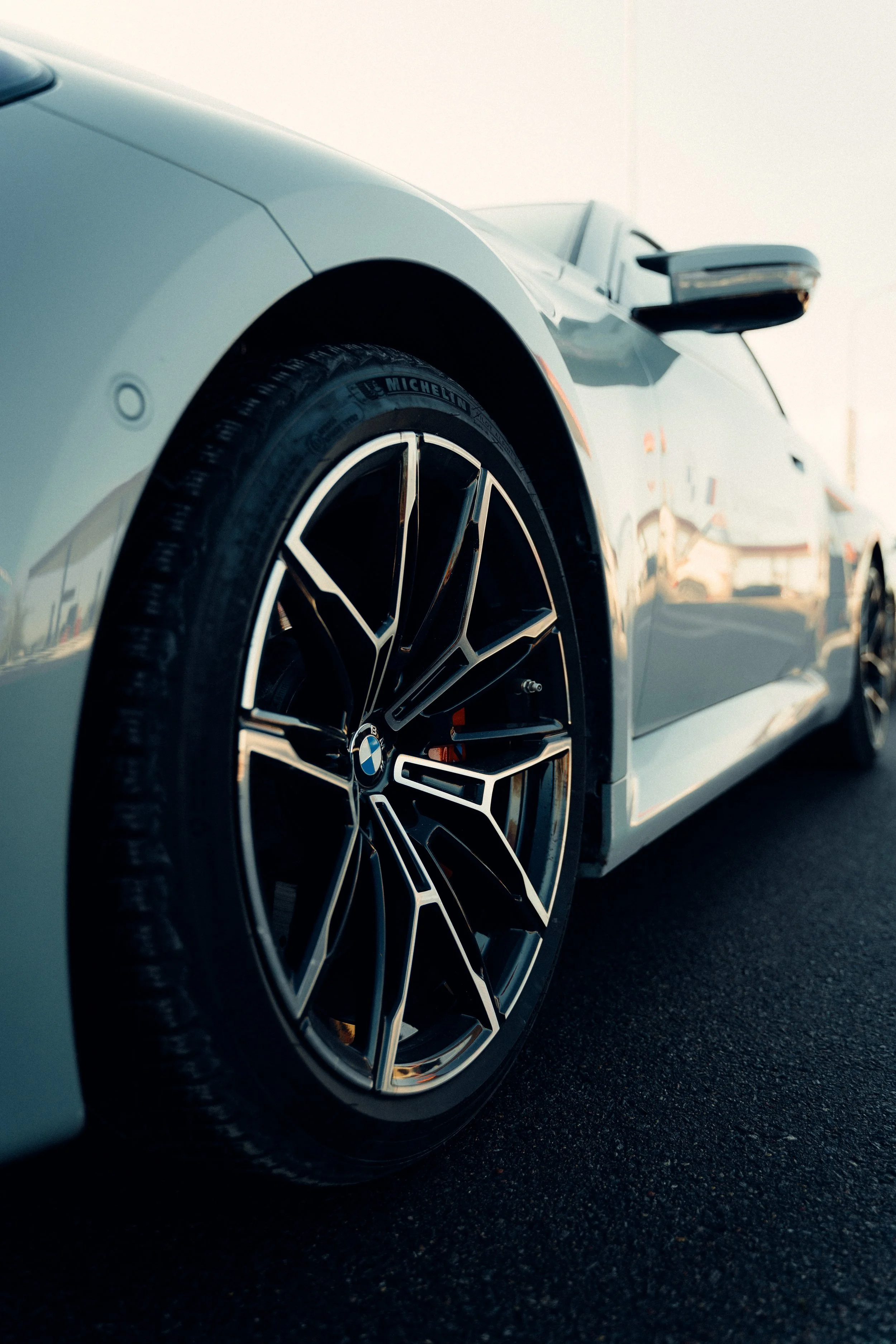 Close-up of a white BMW sports car with black and silver alloy wheels on a dark road.
