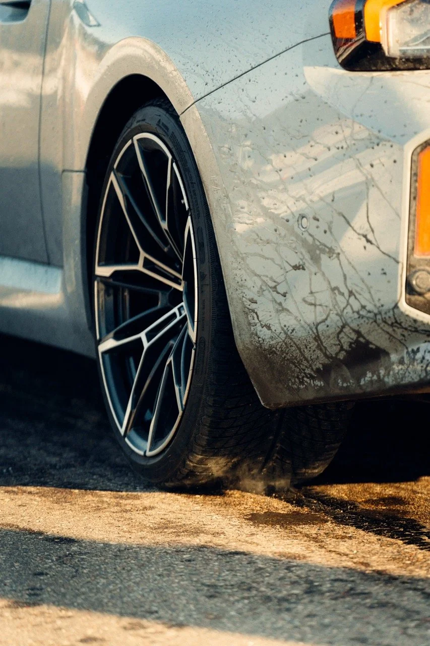 Close-up of a silver car's front wheel on asphalt, with dirt and tire smoke visible.
