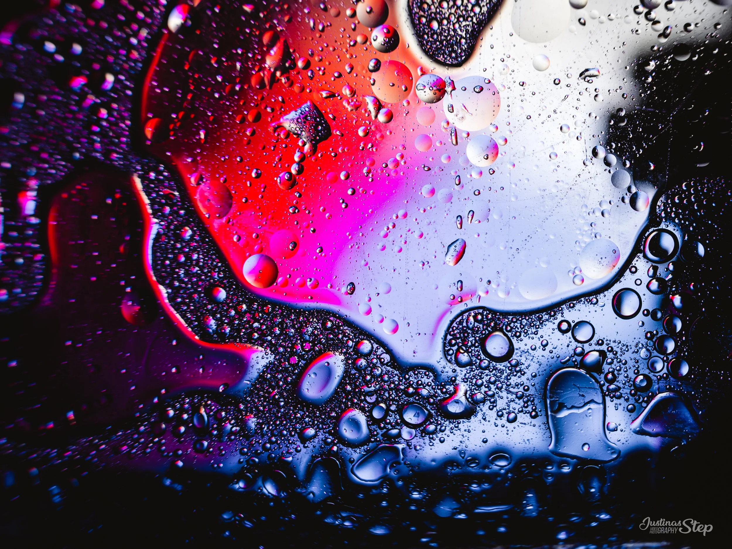 Close-up of colorful oil and water droplets on glass with pink, purple, black, and white background.