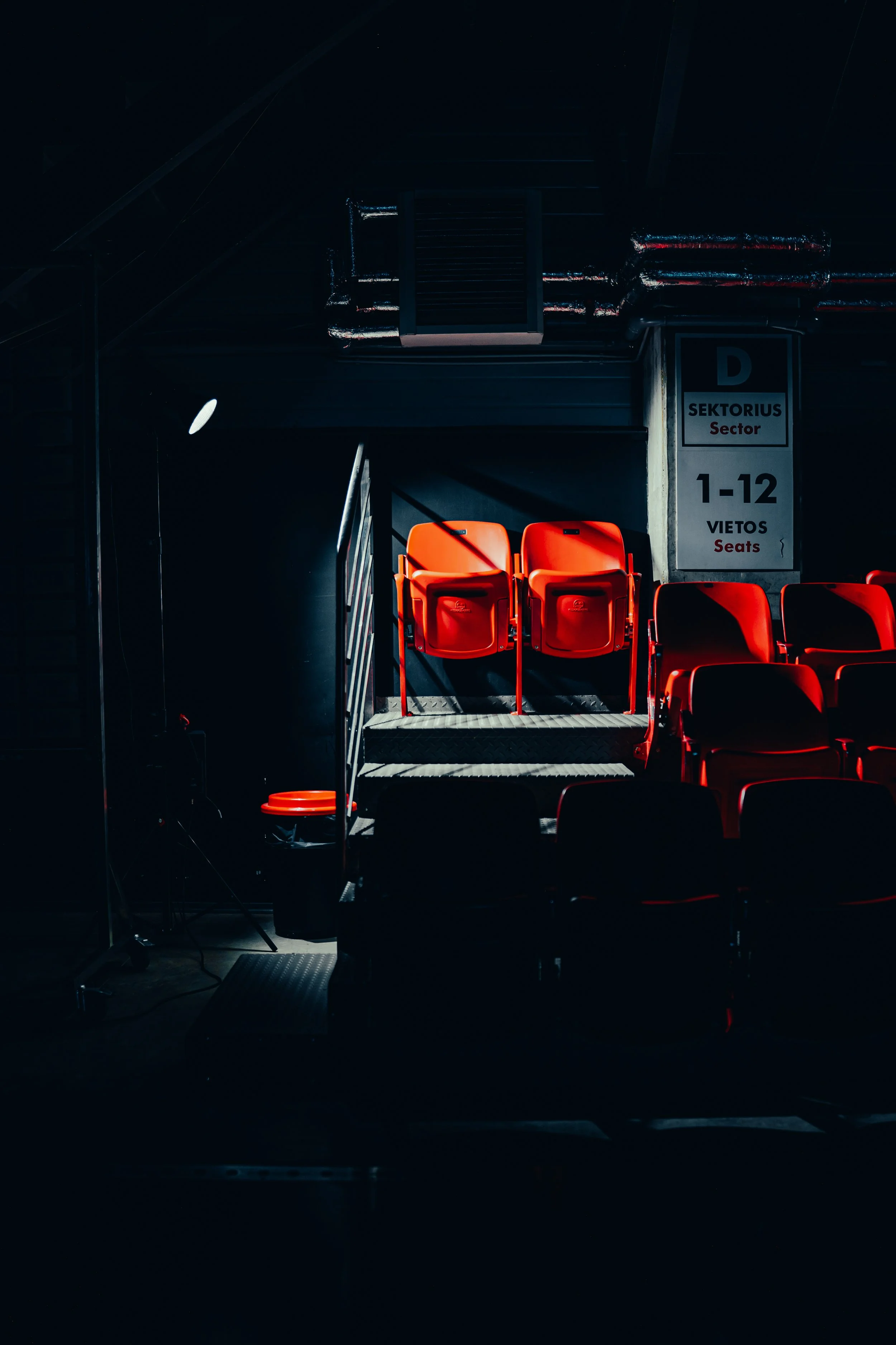 Empty red seats in a mostly dark stadium section labeled D, sector, with seating for numbers 1-12, signs in both English and another language.