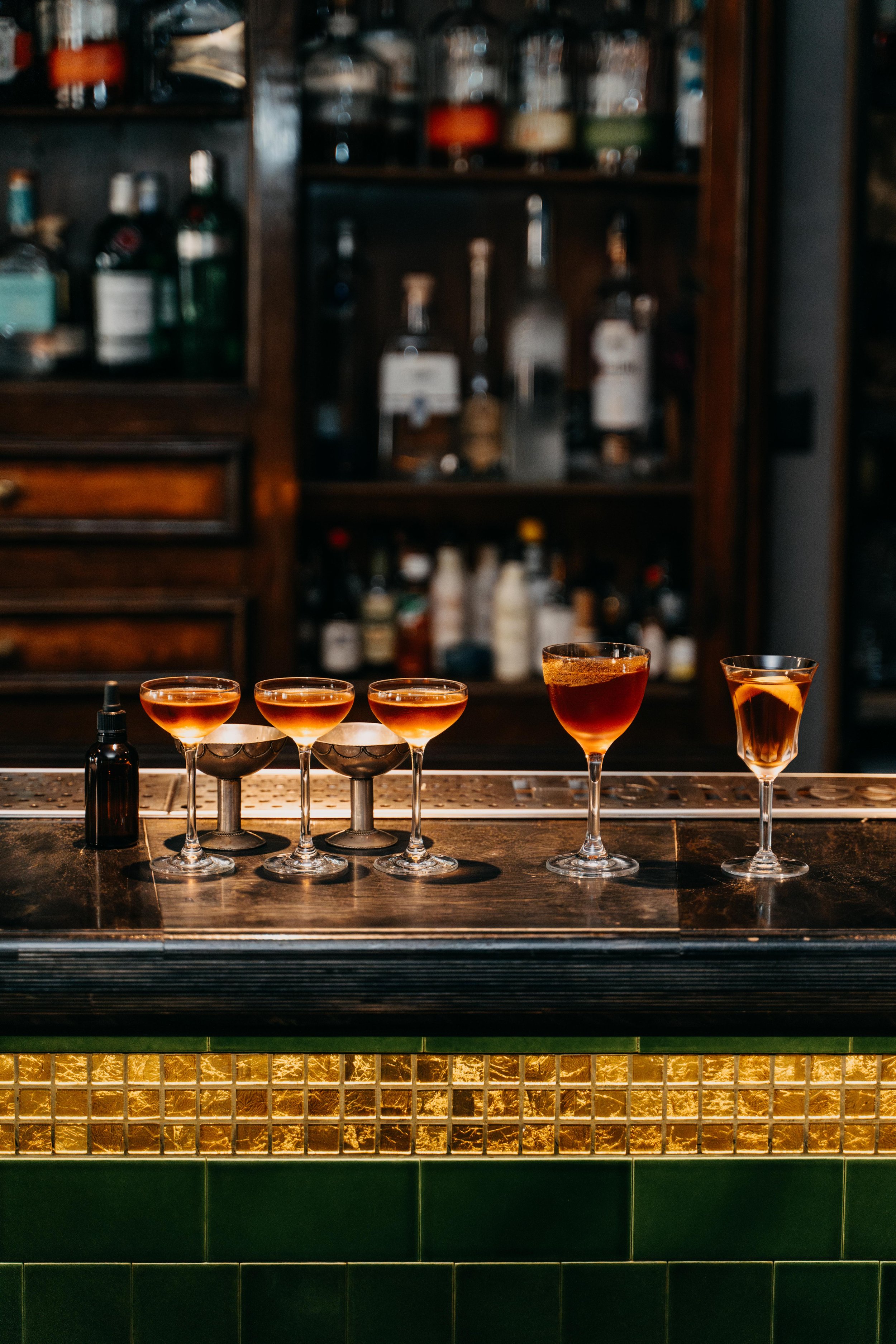 Assorted cocktail glasses on a bar counter with liquor bottles in the background.