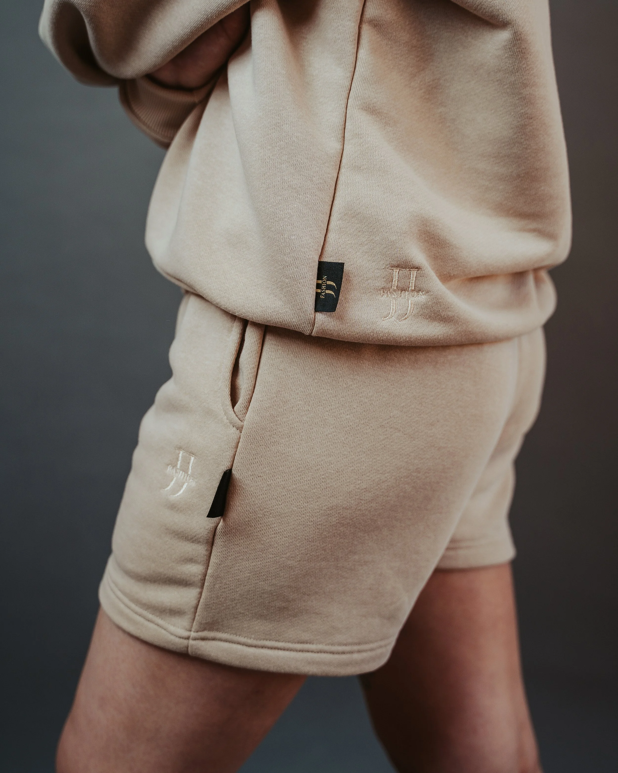 Close-up of beige sweatshirt and shorts with black tags and white embroidered design.