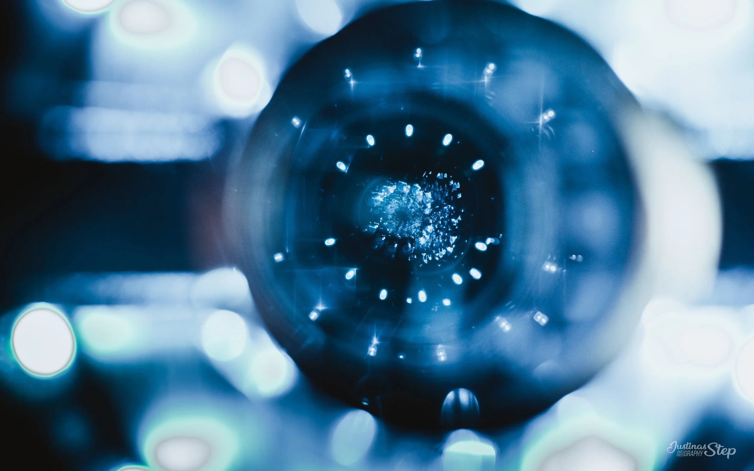 Close-up photograph of a metallic object with a circular opening, illuminated by blue light, showing a perspective from the front, with bokeh effect in the background.