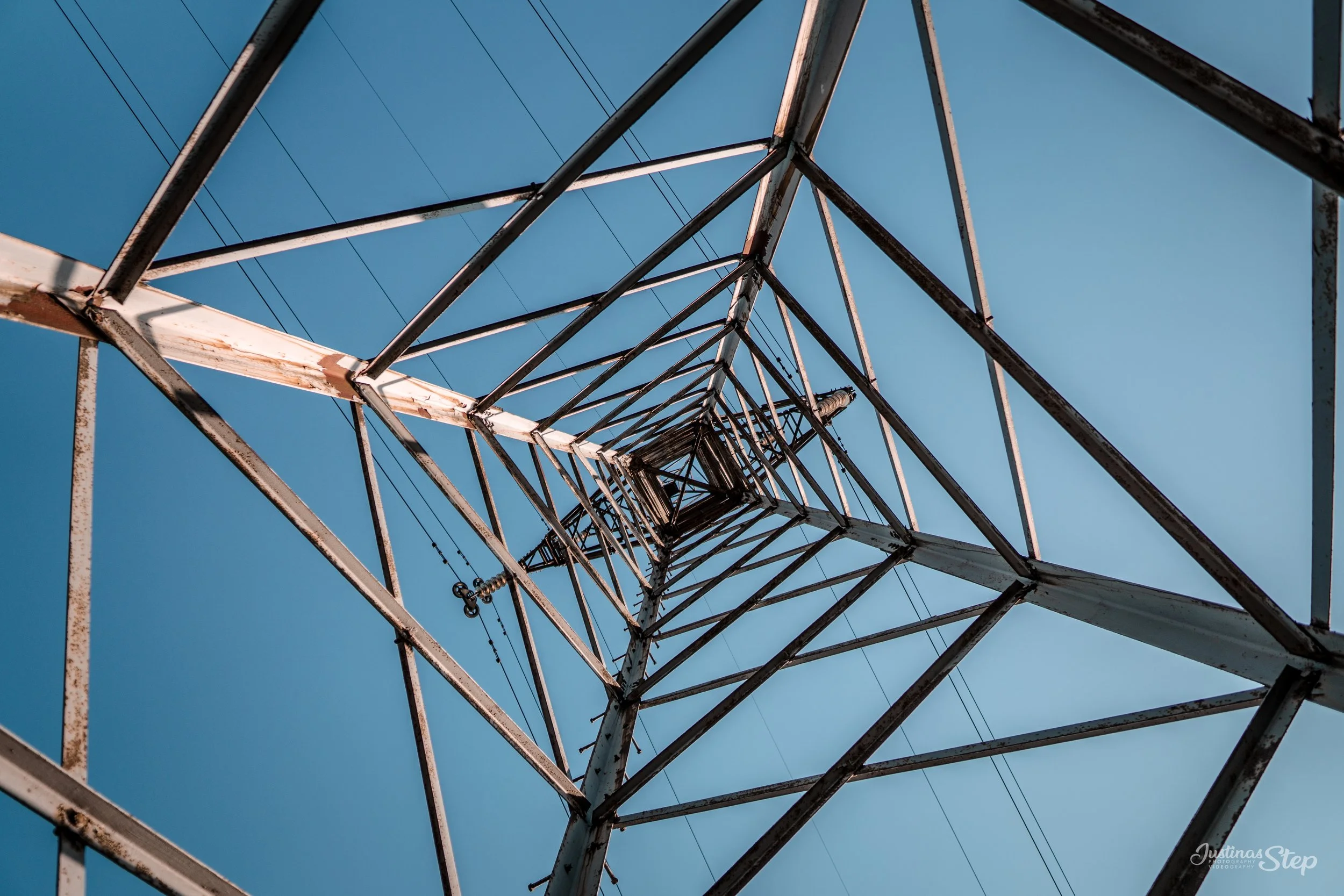 bottom-up view of a tall metal electricity transmission tower against a clear blue sky.