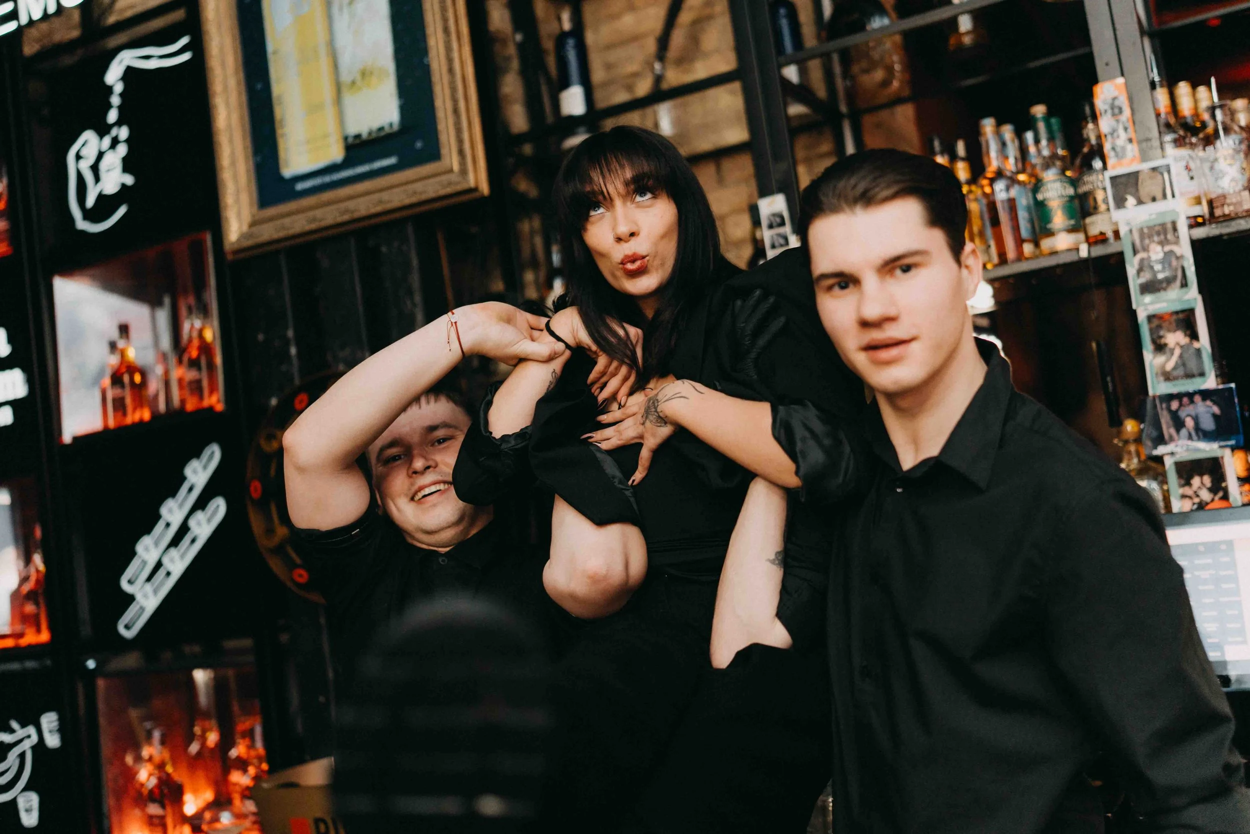 Three friends enjoying drinks at a bar, smiling and posing for the camera.