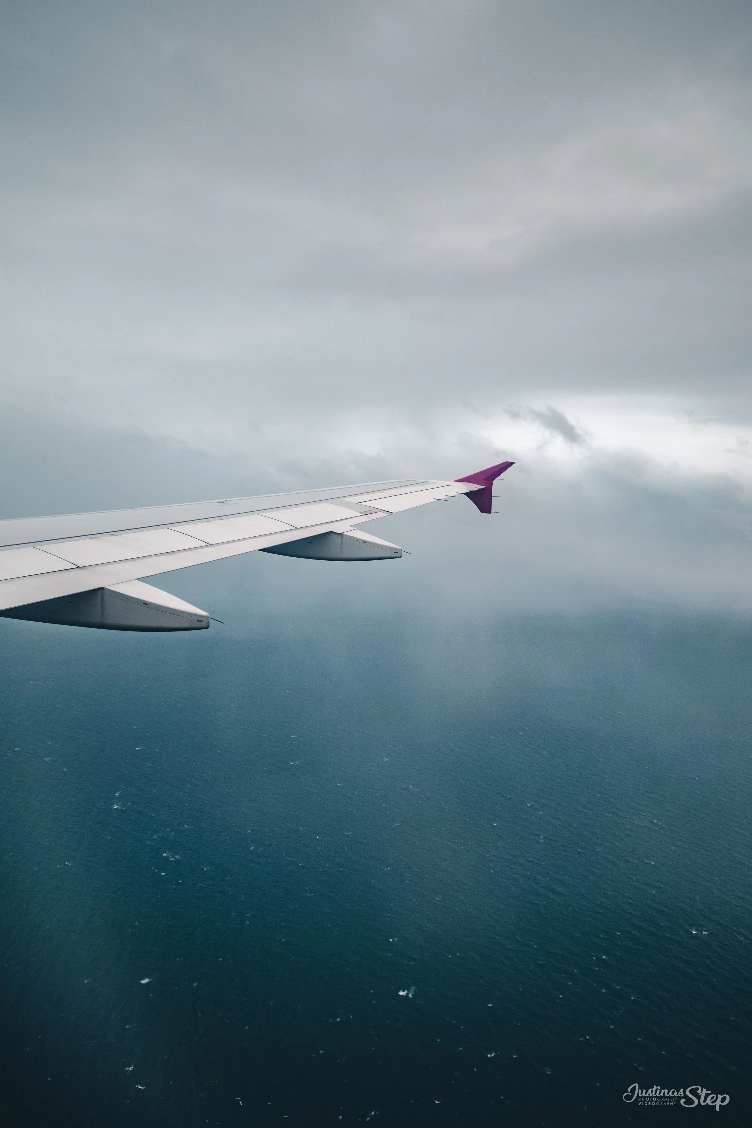 Photo of an airplane wing flying above the ocean under a cloudy sky.