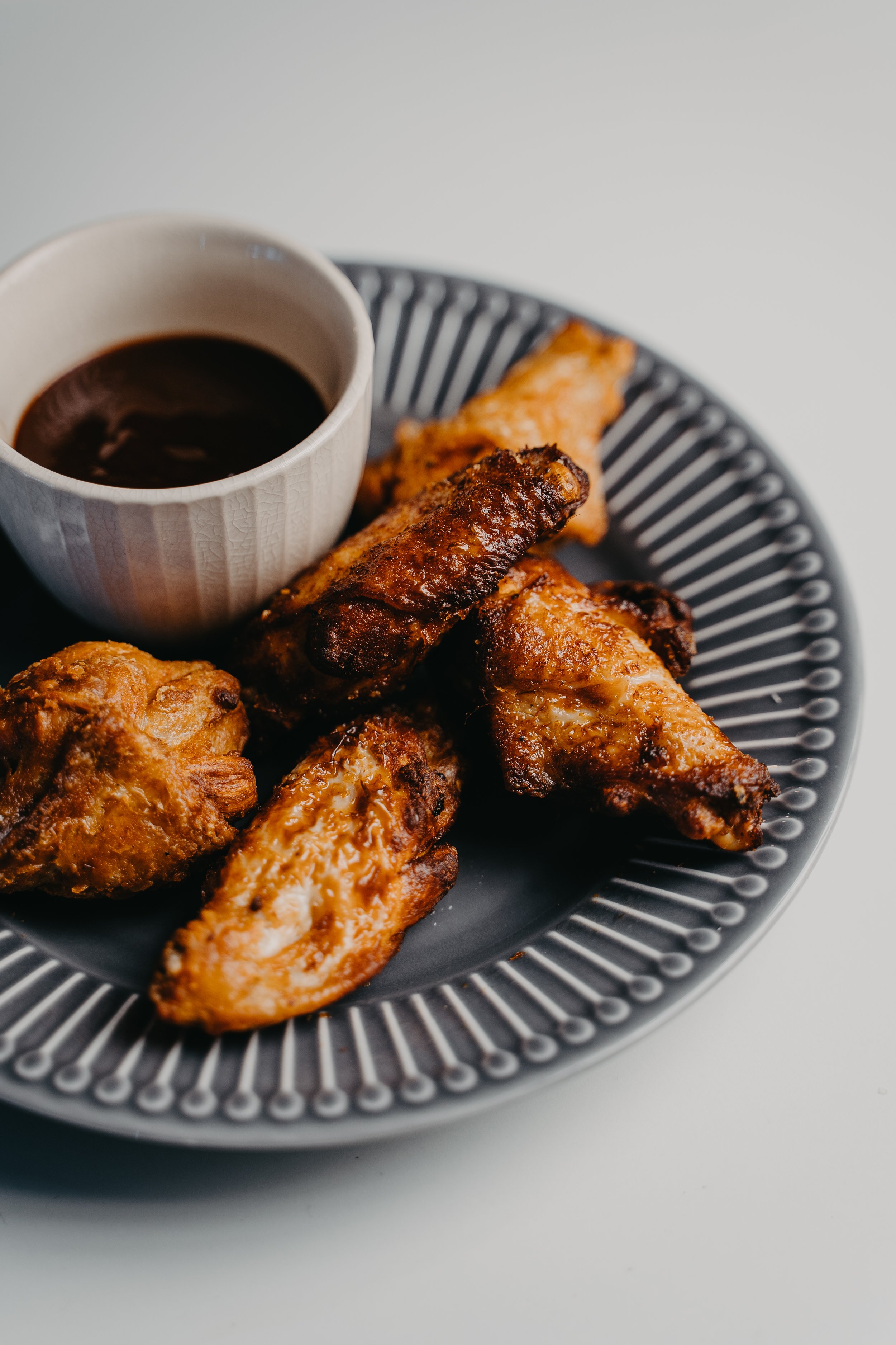A black plate with fried chicken pieces and a small cup of dark dipping sauce.
