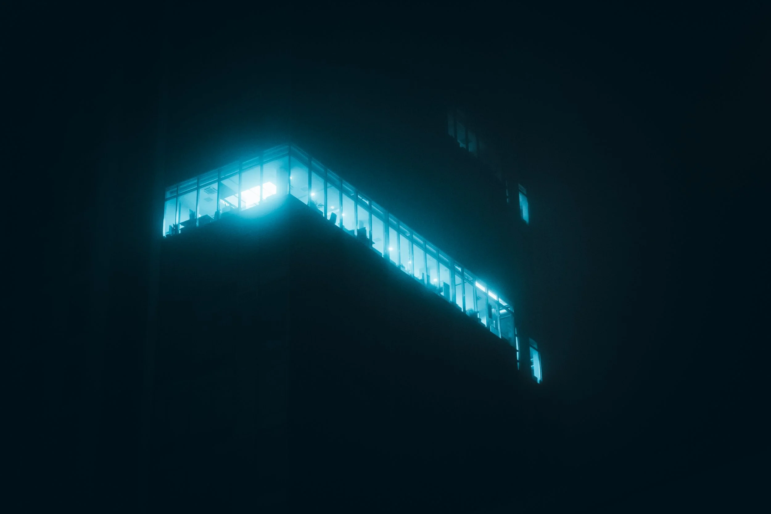 Nighttime photo of a modern building with bright blue lights illuminating its glass windows and balconies, with a dark sky background.