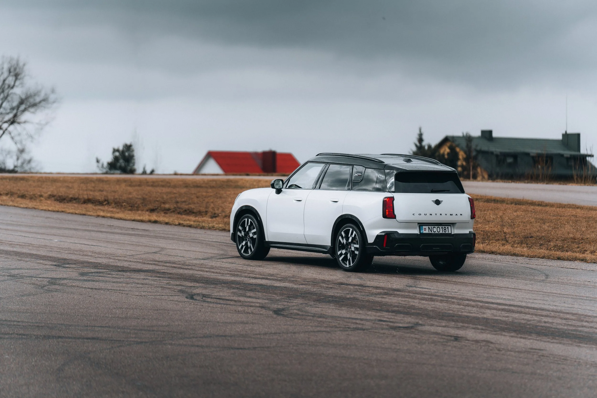 A white electric SUV with black roof parked on a damp road in a rural area under a cloudy sky.