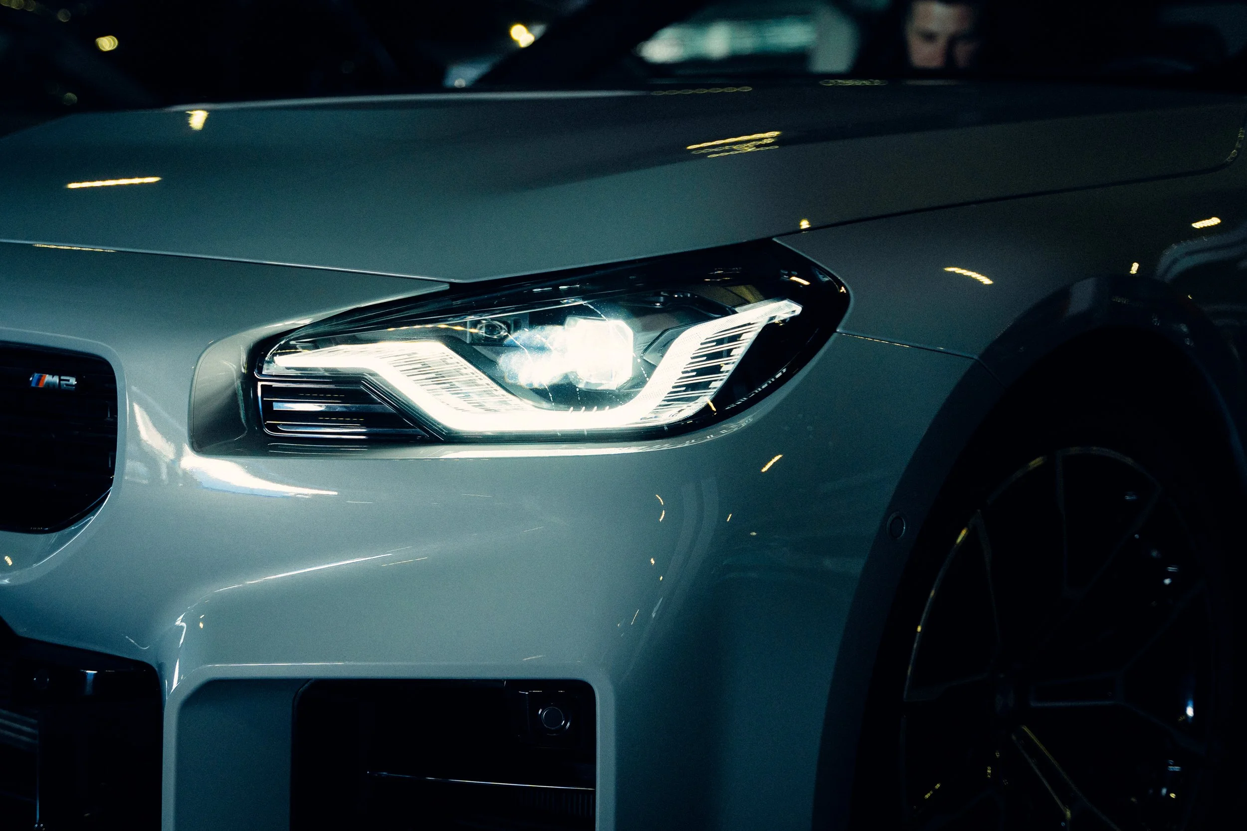 Close-up of a silver modern car's front, highlighting the headlight, grille, and part of the wheel.
