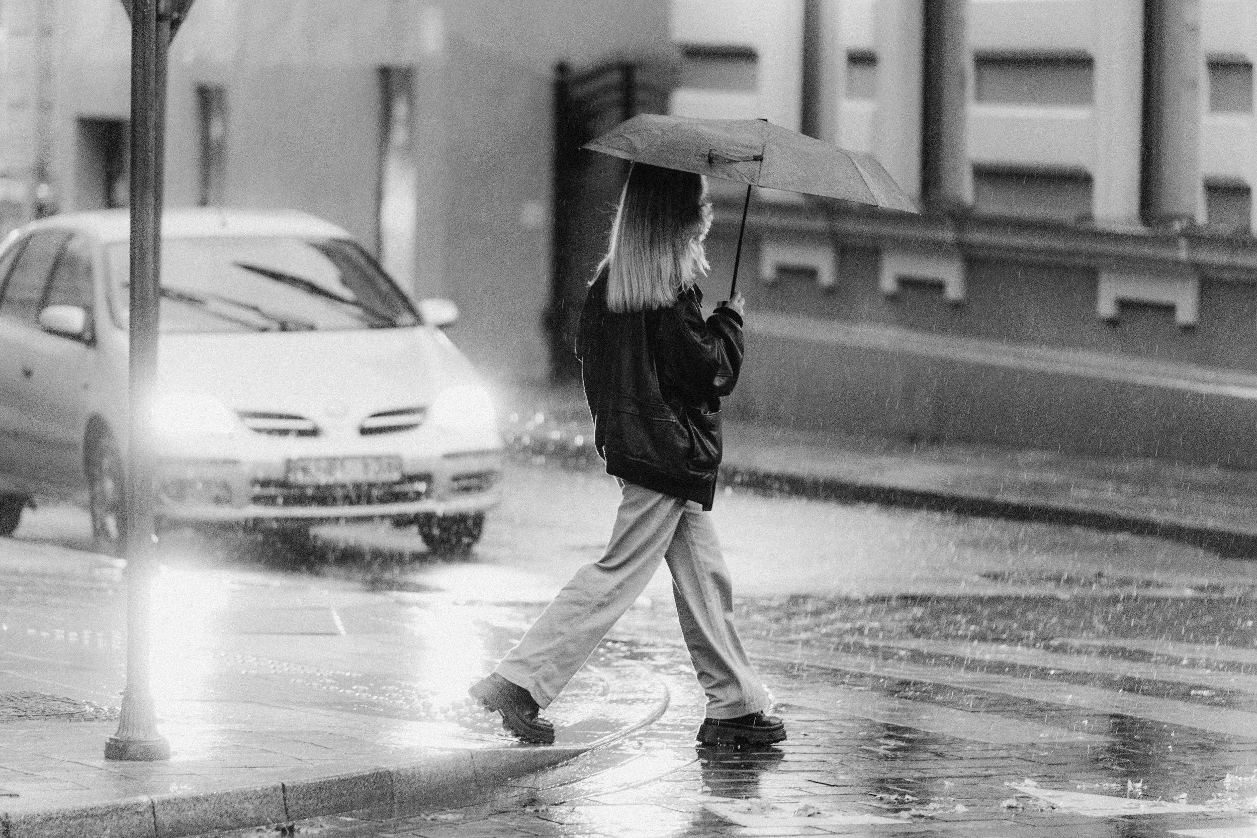 A woman walks with an umbrella on a rainy street in an urban setting.