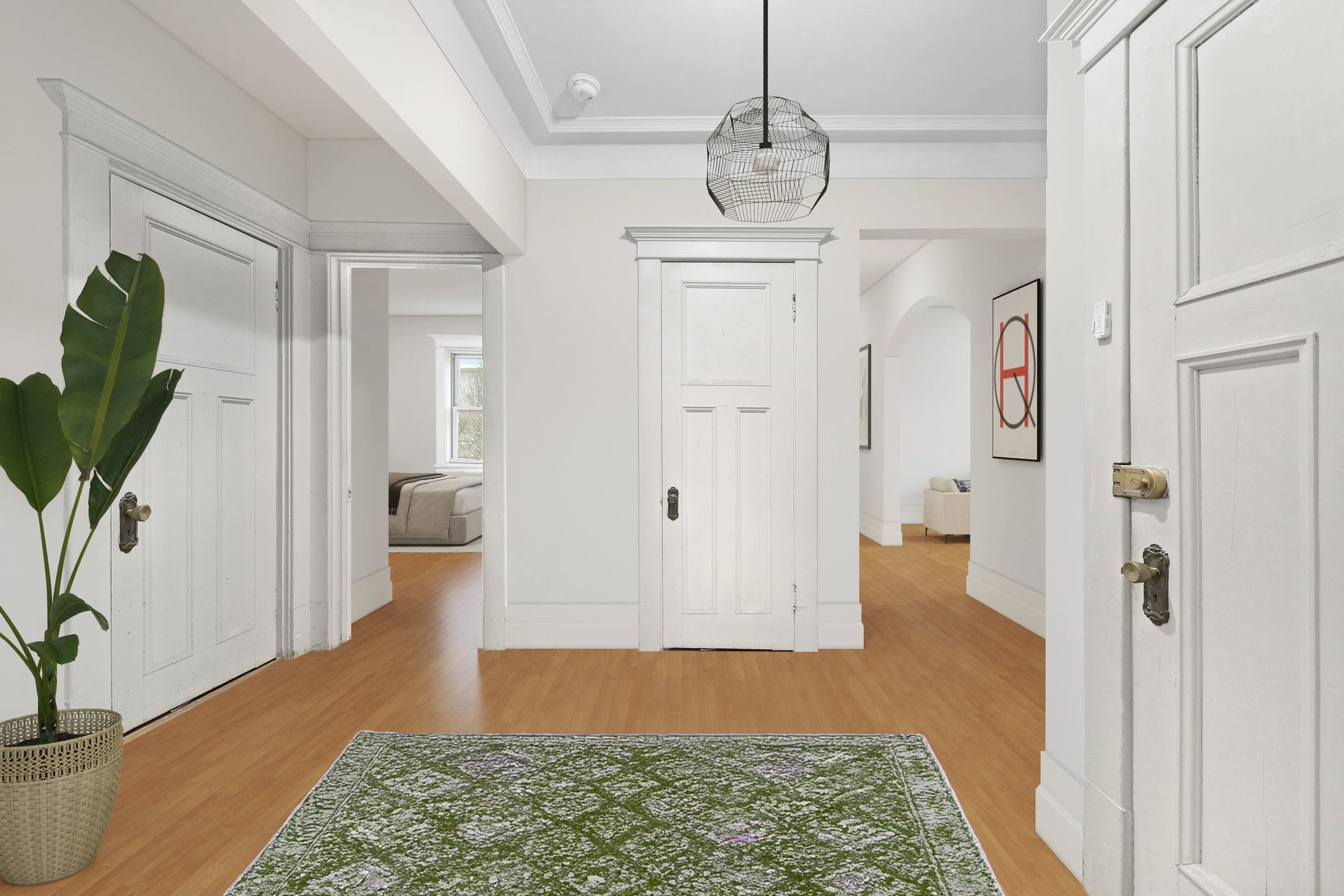 Entryway of a home with white walls, wooden floor, a green patterned rug, a large potted plant on the left, and three white doors with vintage hardware, leading to bedrooms and living space.