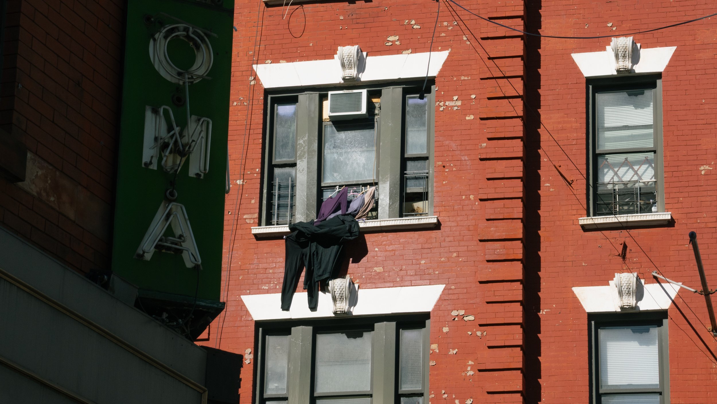 Apartment window with clothes hanging on the ledge and an air conditioning unit above.