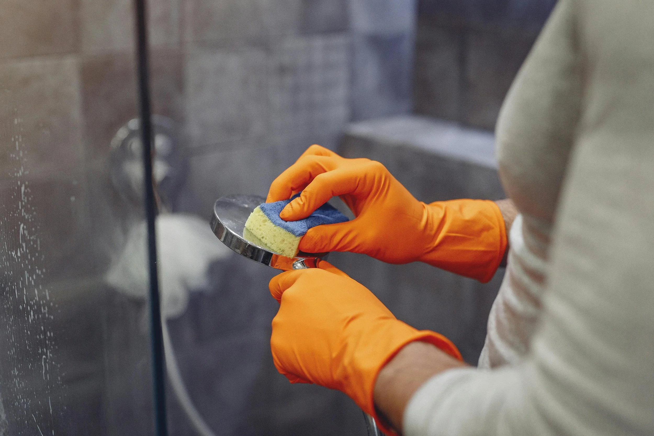 Person wearing orange gloves washing a metal pan with a sponge.