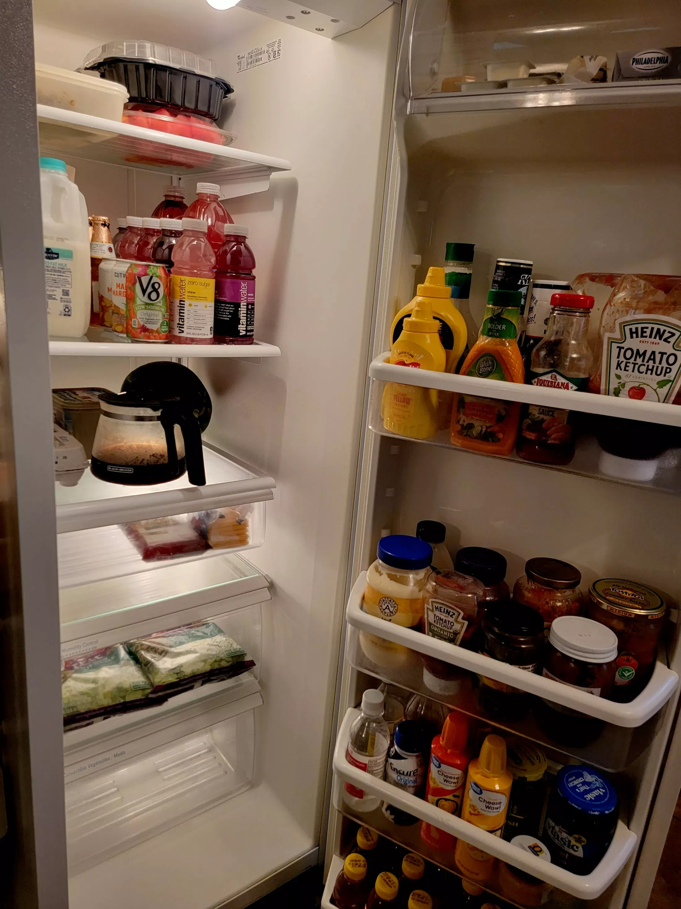 Open refrigerator door revealing shelves stocked with beverages, condiments, jars, packages, and other food items.