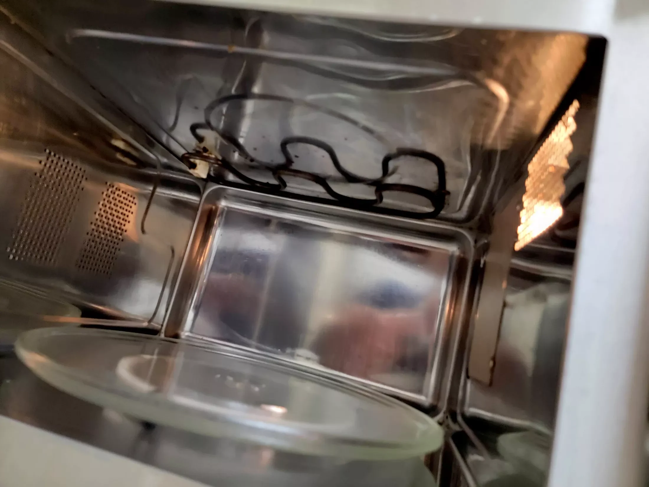 The interior of a stainless steel microwave oven with some wires and a glass plate.