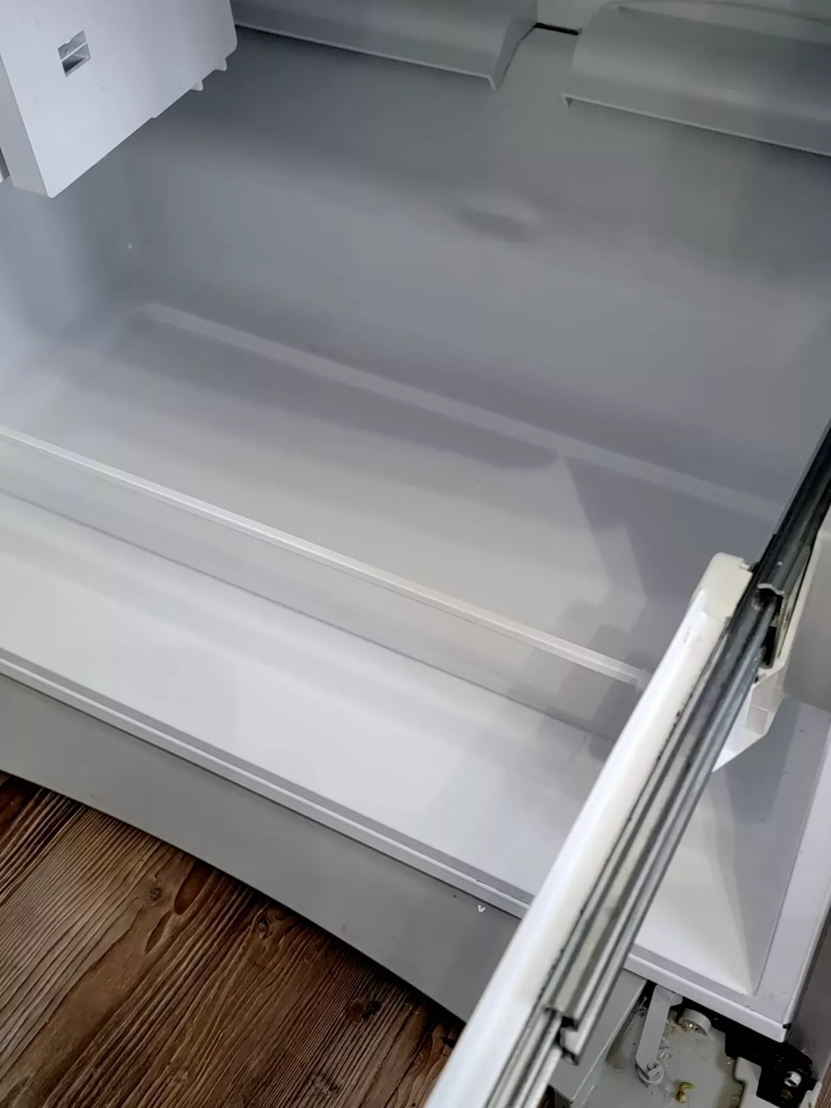 Empty, open refrigerator with a wooden floor beneath.
