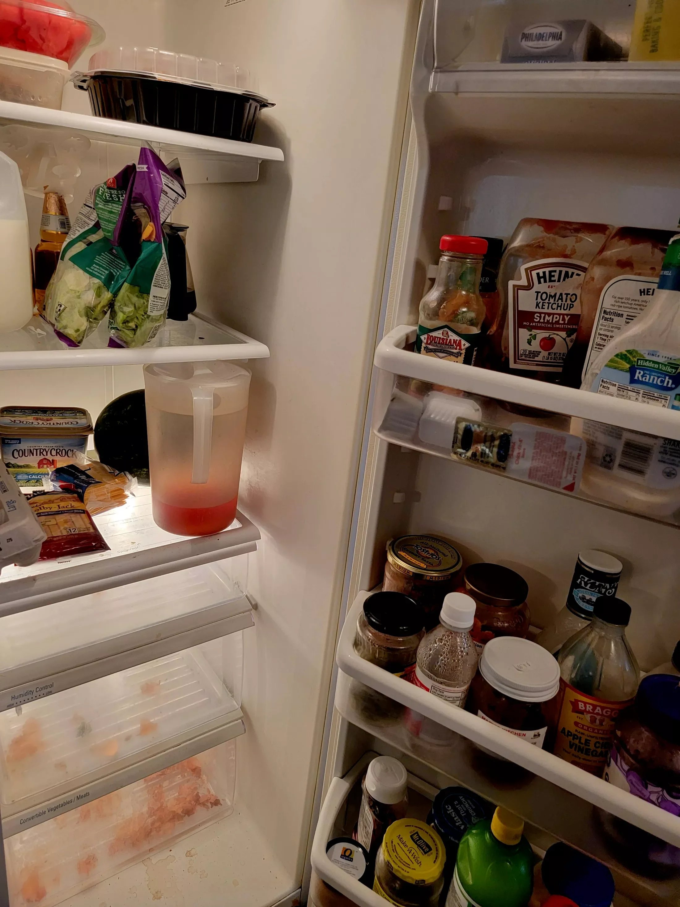 Open refrigerator door showing various condiments, jars, bottles, and food items on shelves, with some items on the refrigerator door and some inside.