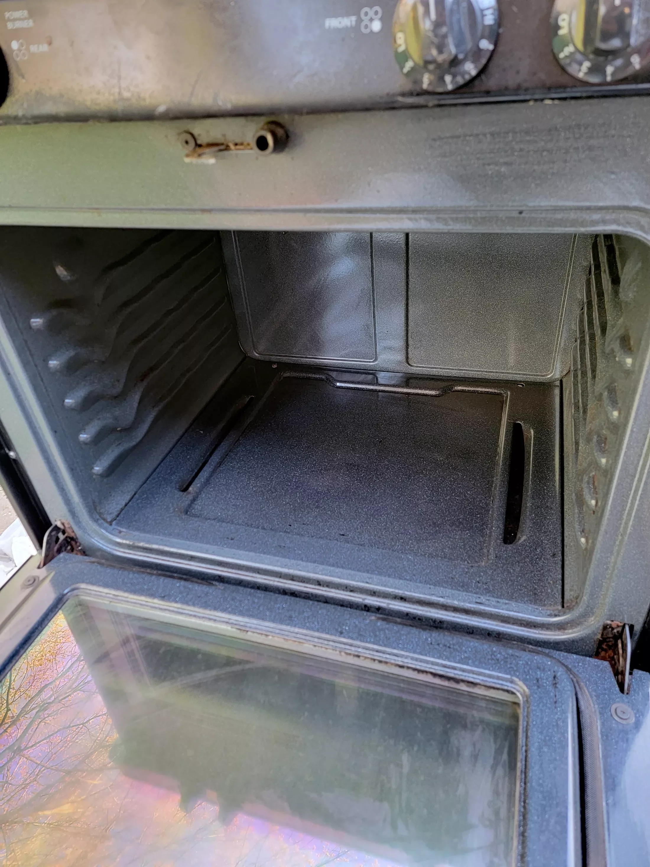 Empty upright oven with open glass door, showing clean interior with racks and controls on top.