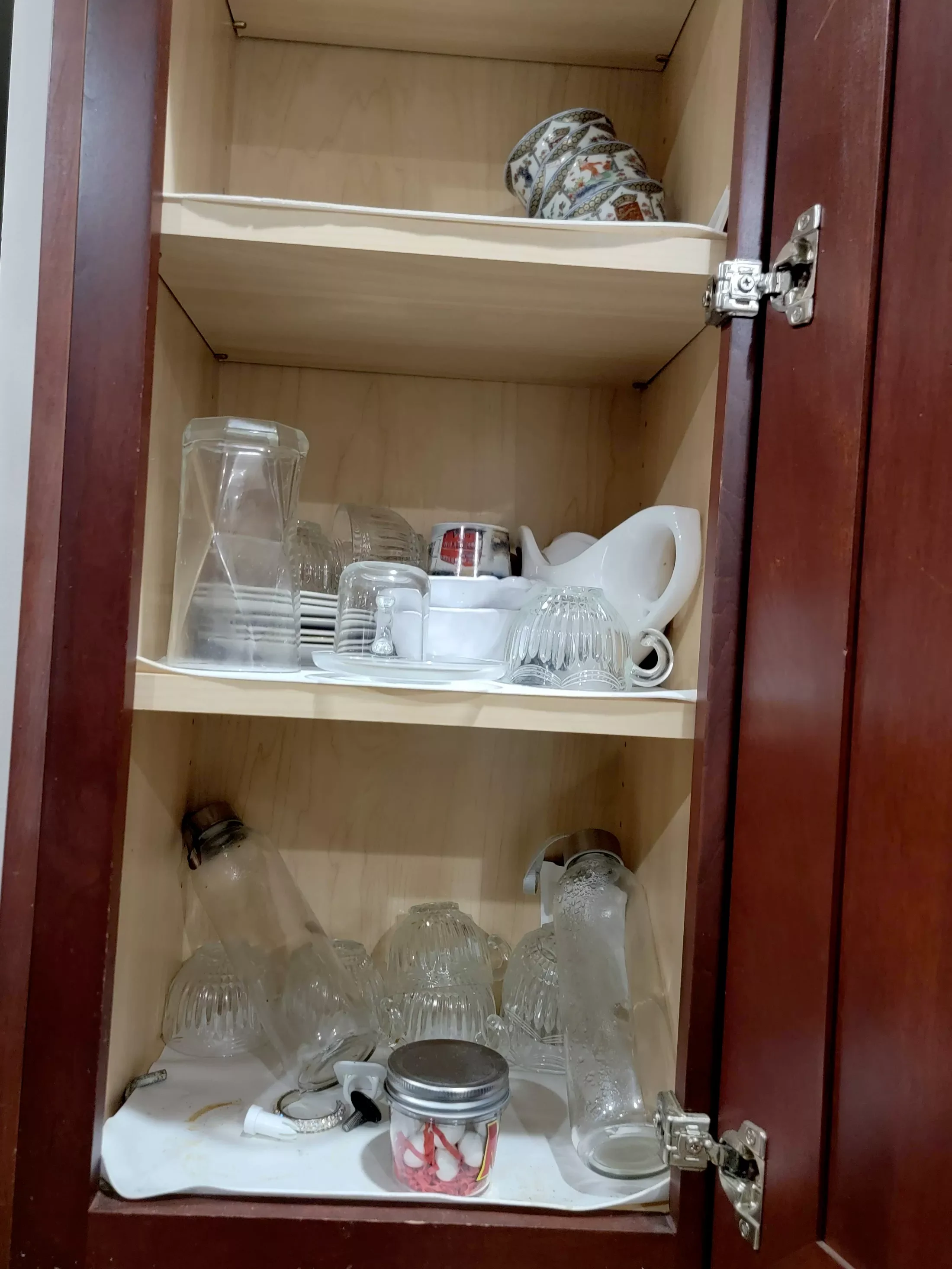 Open kitchen cabinet with shelves containing glassware, mugs, and decorative plates.