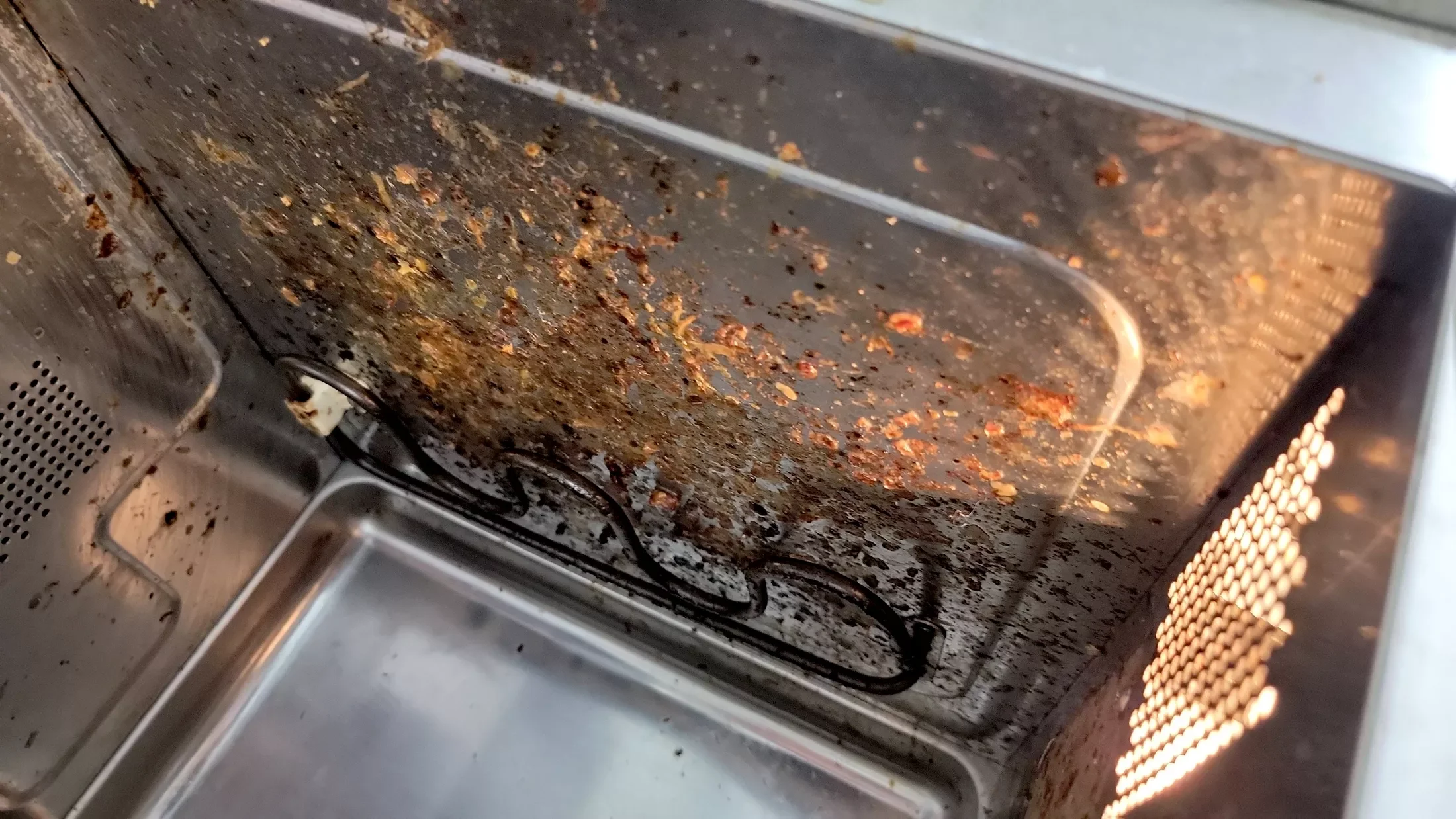 Inside of a microwave oven with food splatters and burnt debris on the ceiling and walls, including the turntable and heating element.
