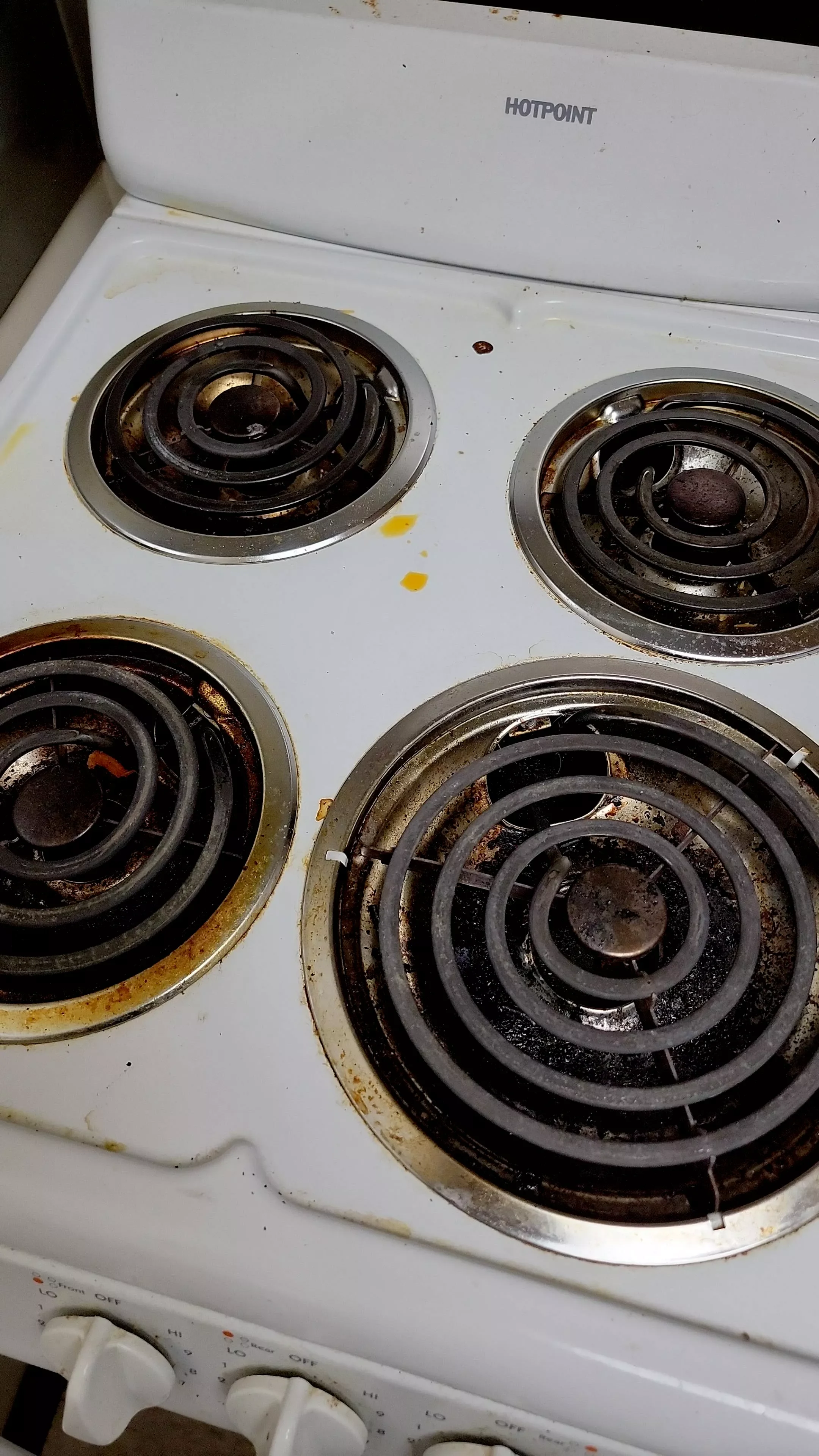 Dirty, stained stovetop with four coil burners and discolored white surface.