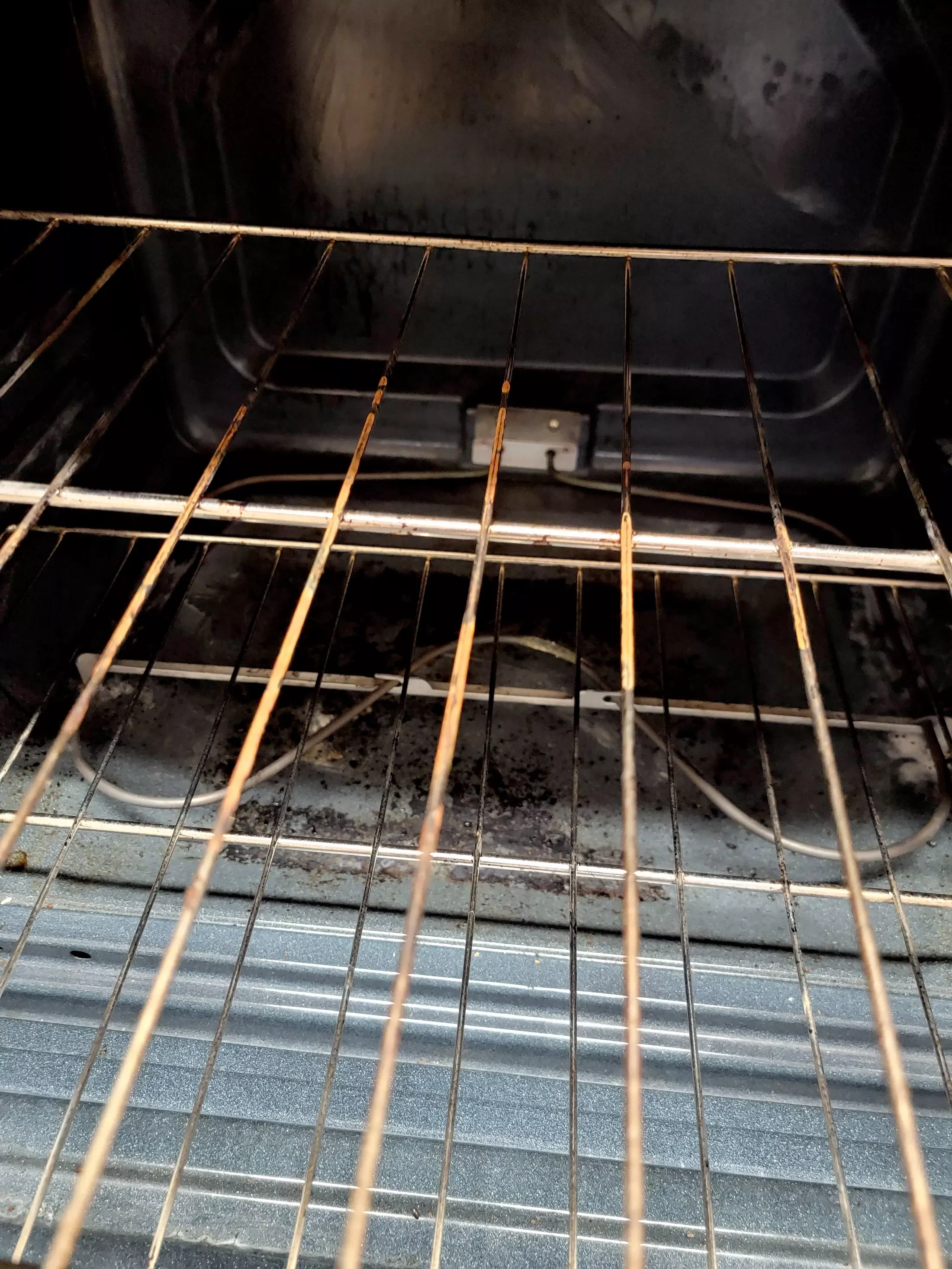 Inside of a rusty oven with a heating element and oven racks
