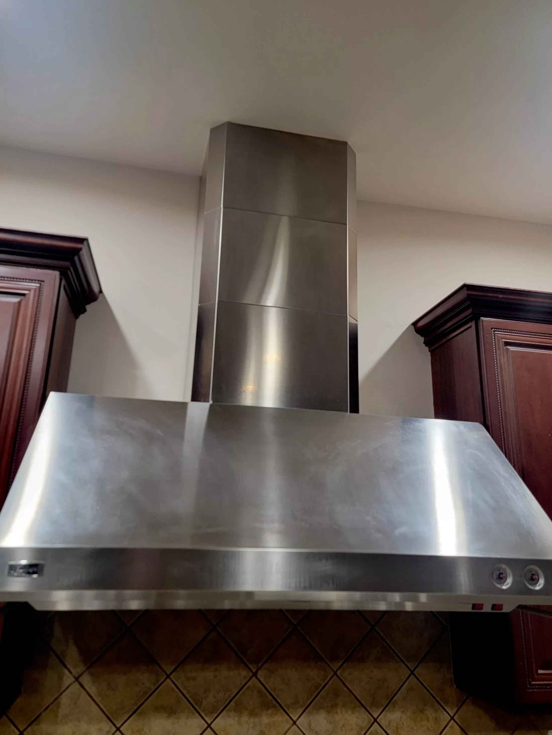 Stainless steel range hood installed between dark wooden cabinets in a kitchen.