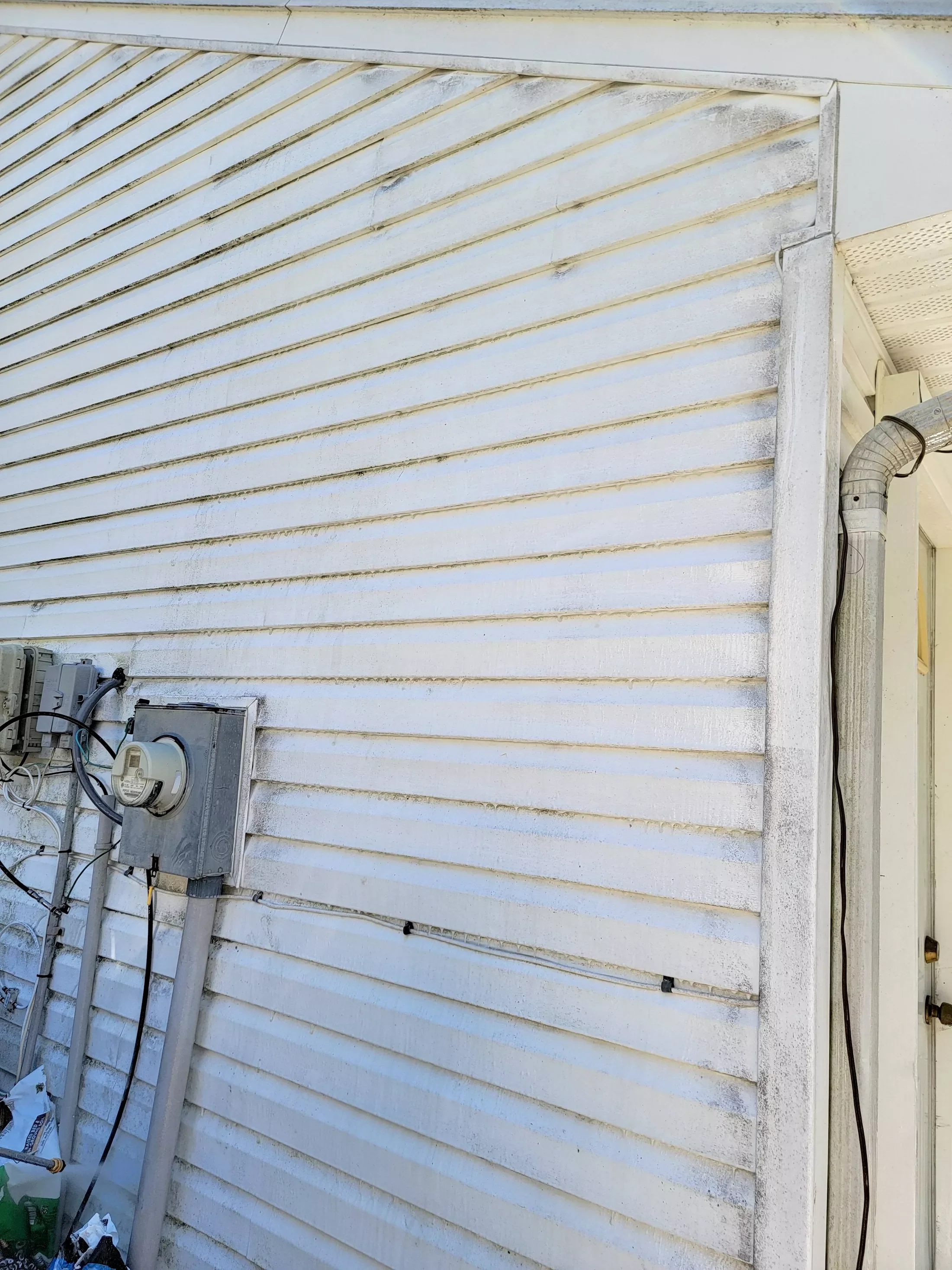 Close-up of a white house exterior with vinyl siding, electrical meter, and electrical wires, showing some dirt and weathering.