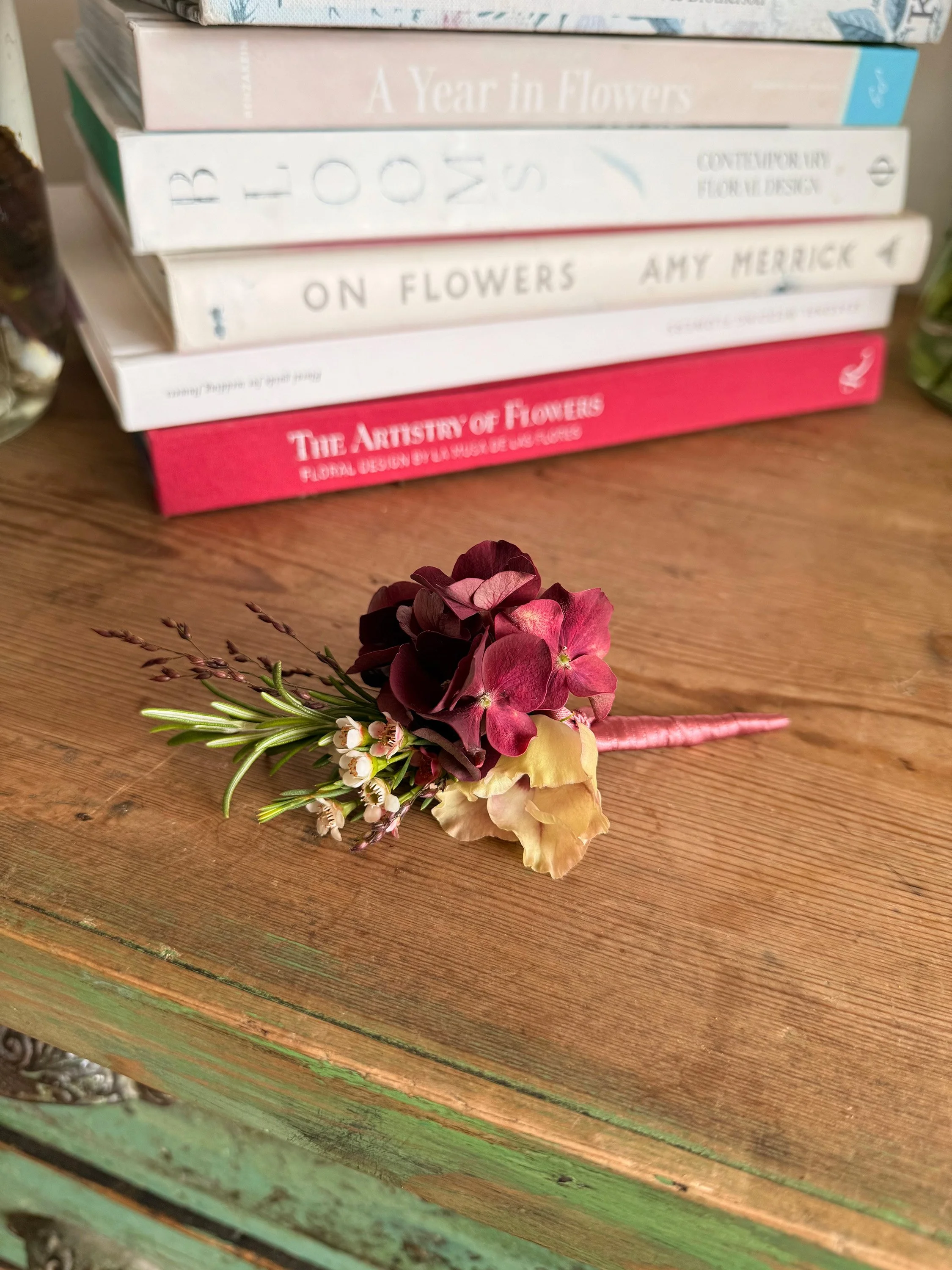 A small arrangement of flowers with pink, cream, and dark purple petals, placed on a wooden surface.