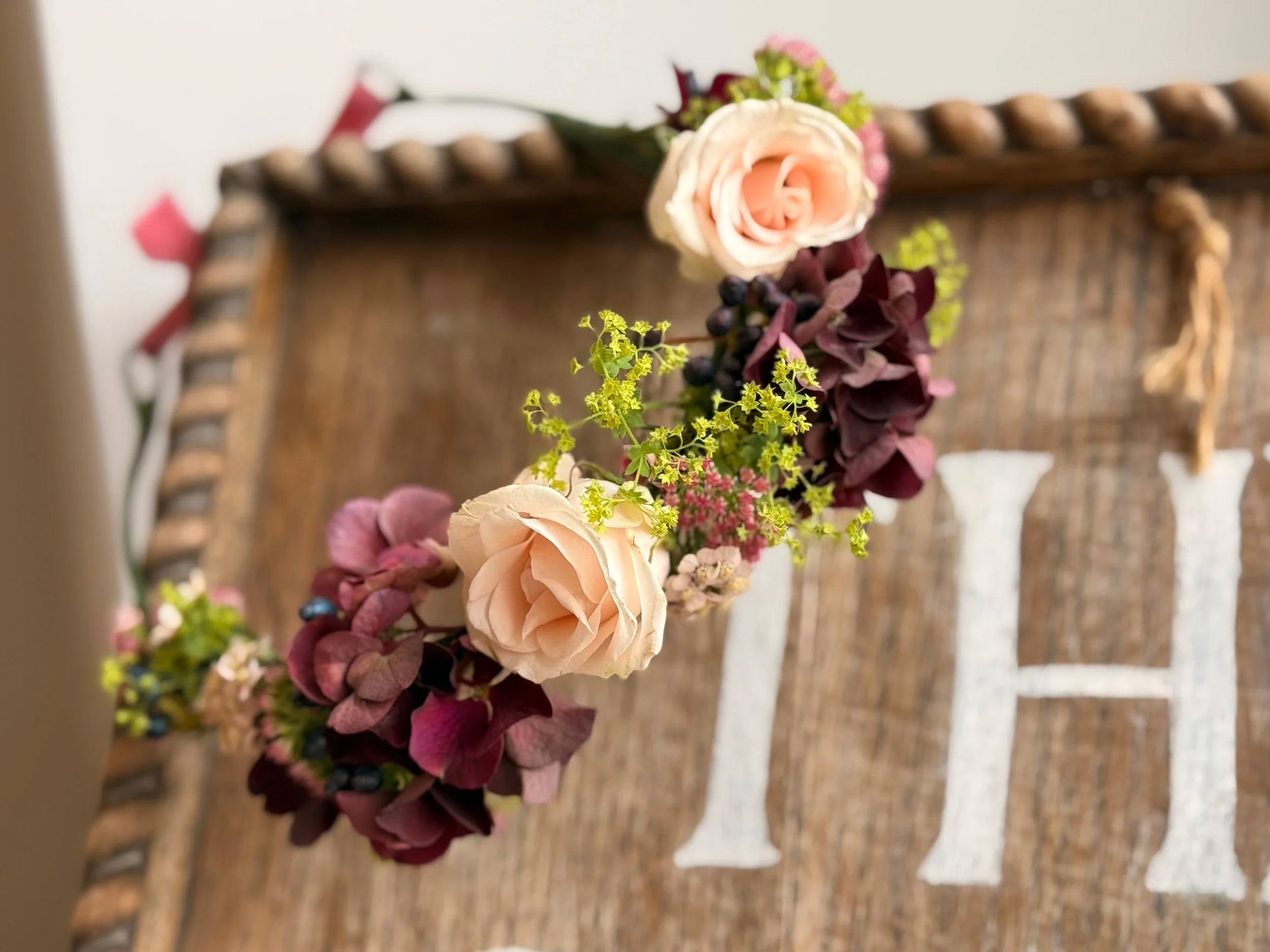 Close-up of a floral centerpiece with pink and white roses, purple and green foliage, placed on a rustic wooden table.