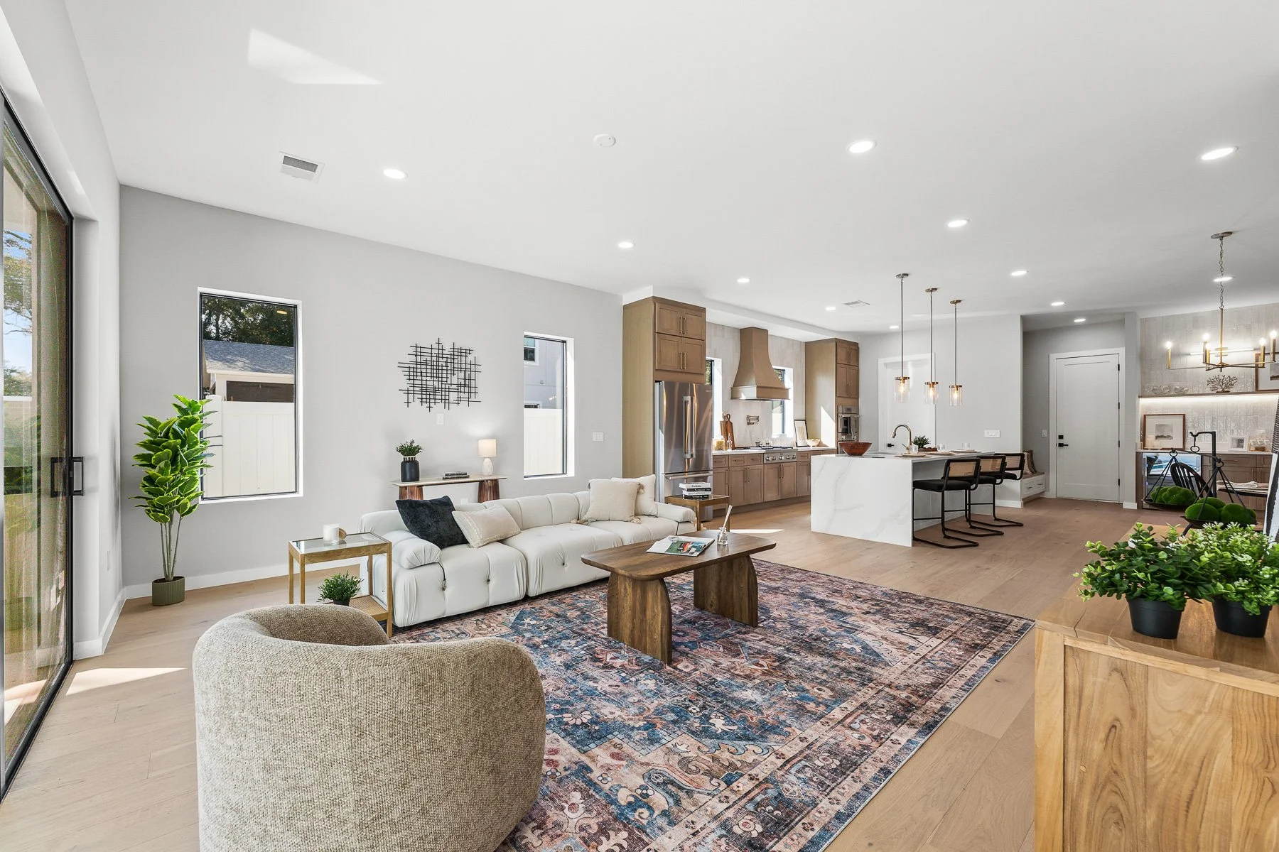 Modern kitchen with white cabinetry, a marble island with seating, stainless steel refrigerator, open shelving, and three pendant lights above the island.