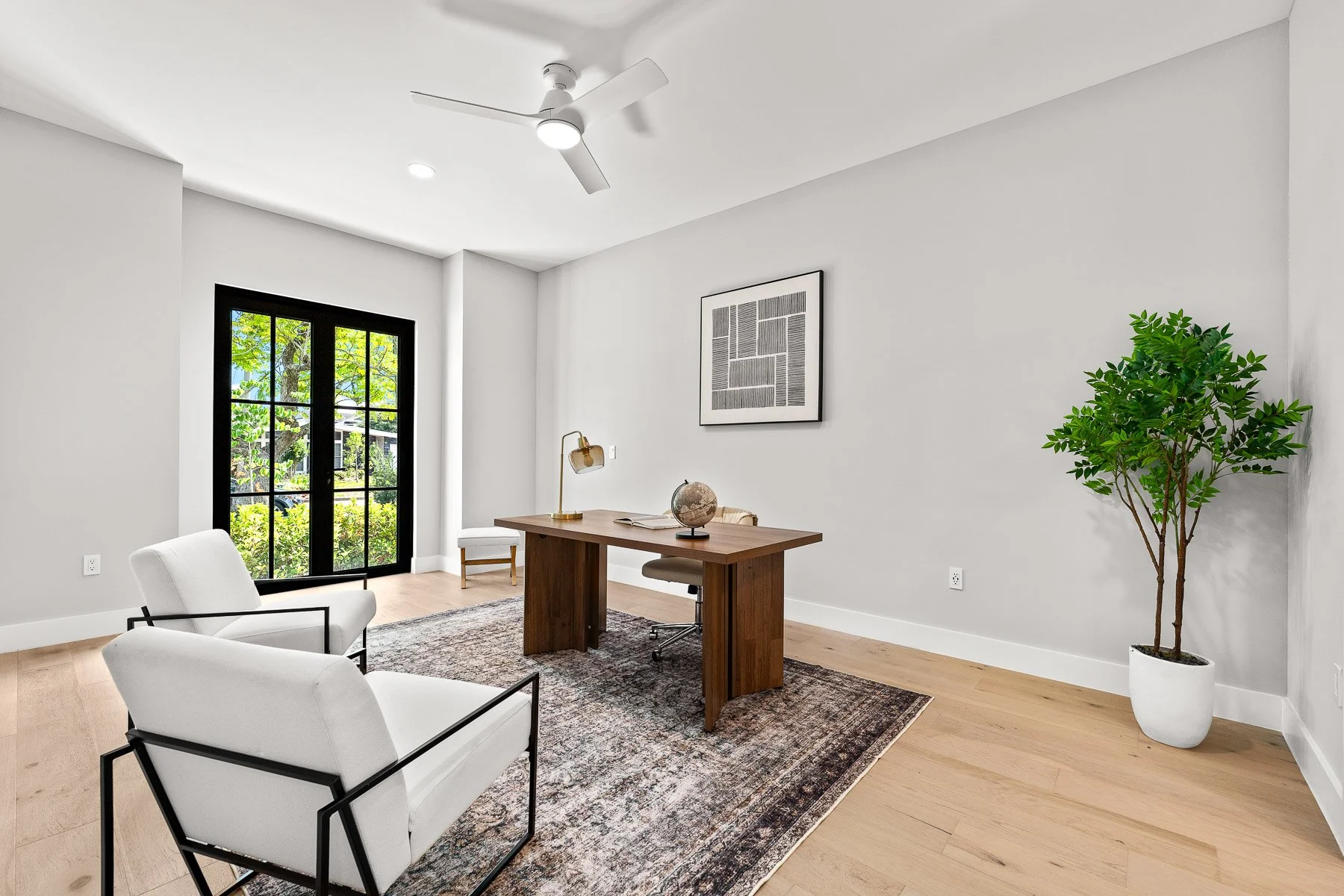 Modern bedroom with three tall black-framed windows, a light gray wall, a wooden dresser, bed with gray and black pillows, and an abstract wall art.