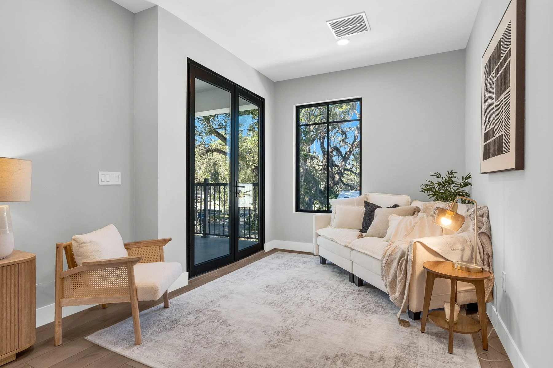 Open-concept living and dining area with wooden flooring, modern furniture, and large windows letting in natural light.