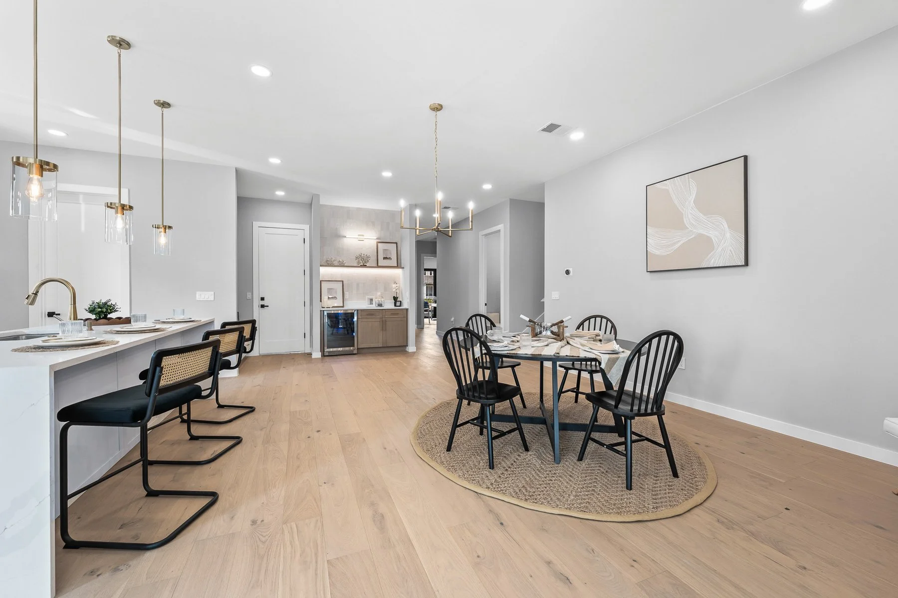 Bright bedroom with four large black-framed windows, light gray walls, a bed with gray bedding and throw pillows, nightstands with lamps, a wooden dresser, and a small bench near the window.