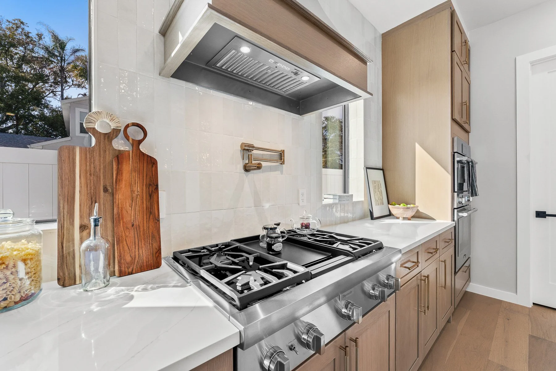 Modern bedroom with three tall black-framed windows, a light gray wall, a wooden dresser, bed with gray and black pillows, and an abstract wall art.