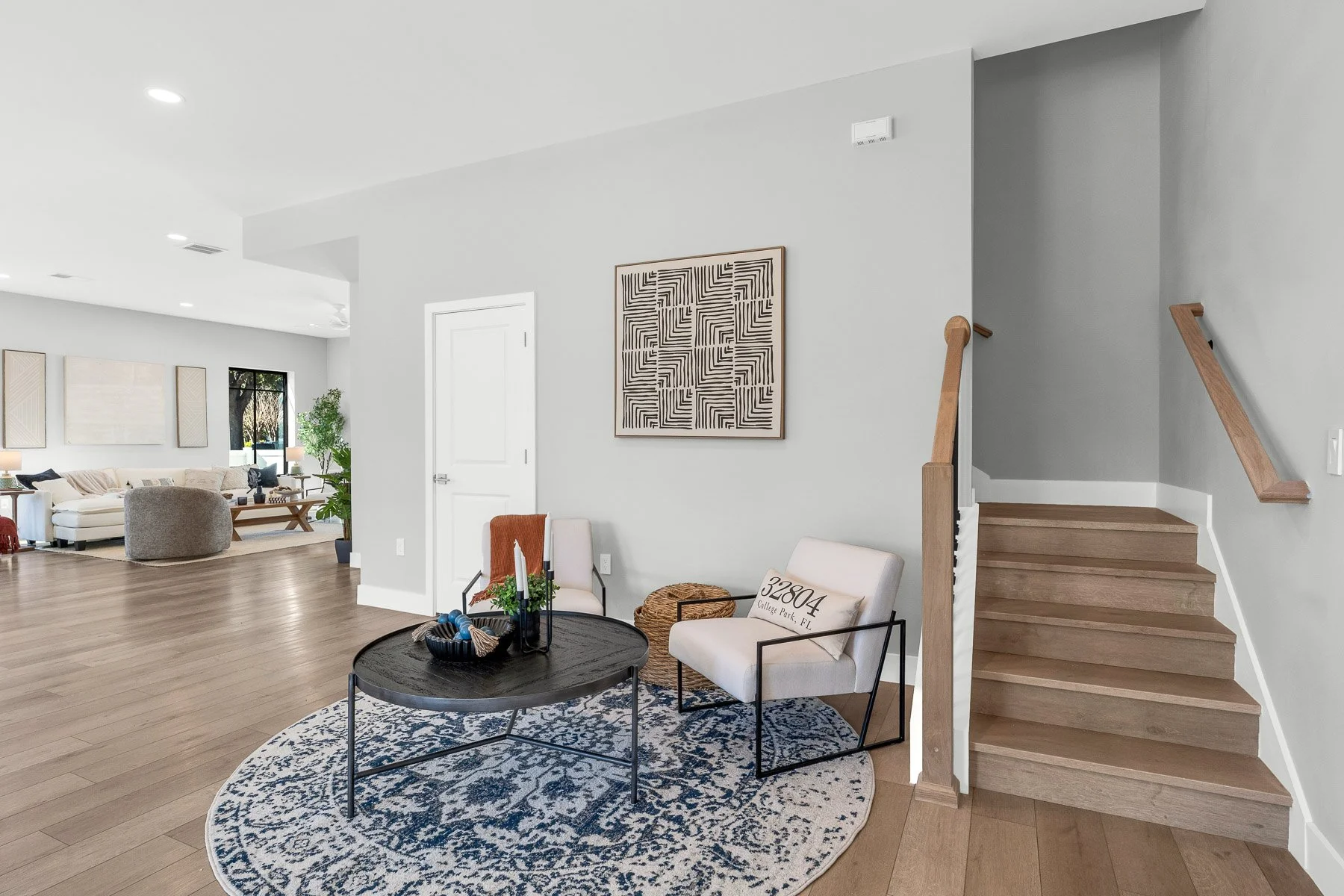Modern bedroom with three tall black-framed windows, a light gray wall, a wooden dresser, bed with gray and black pillows, and an abstract wall art.