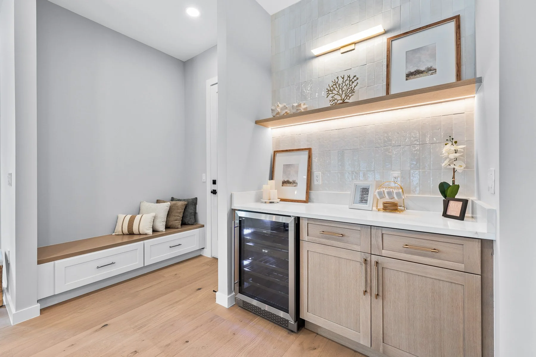 Modern home office with a wooden desk, two rattan chairs, large window, abstract art on wall, potted plant, and a patterned rug on hardwood floor.