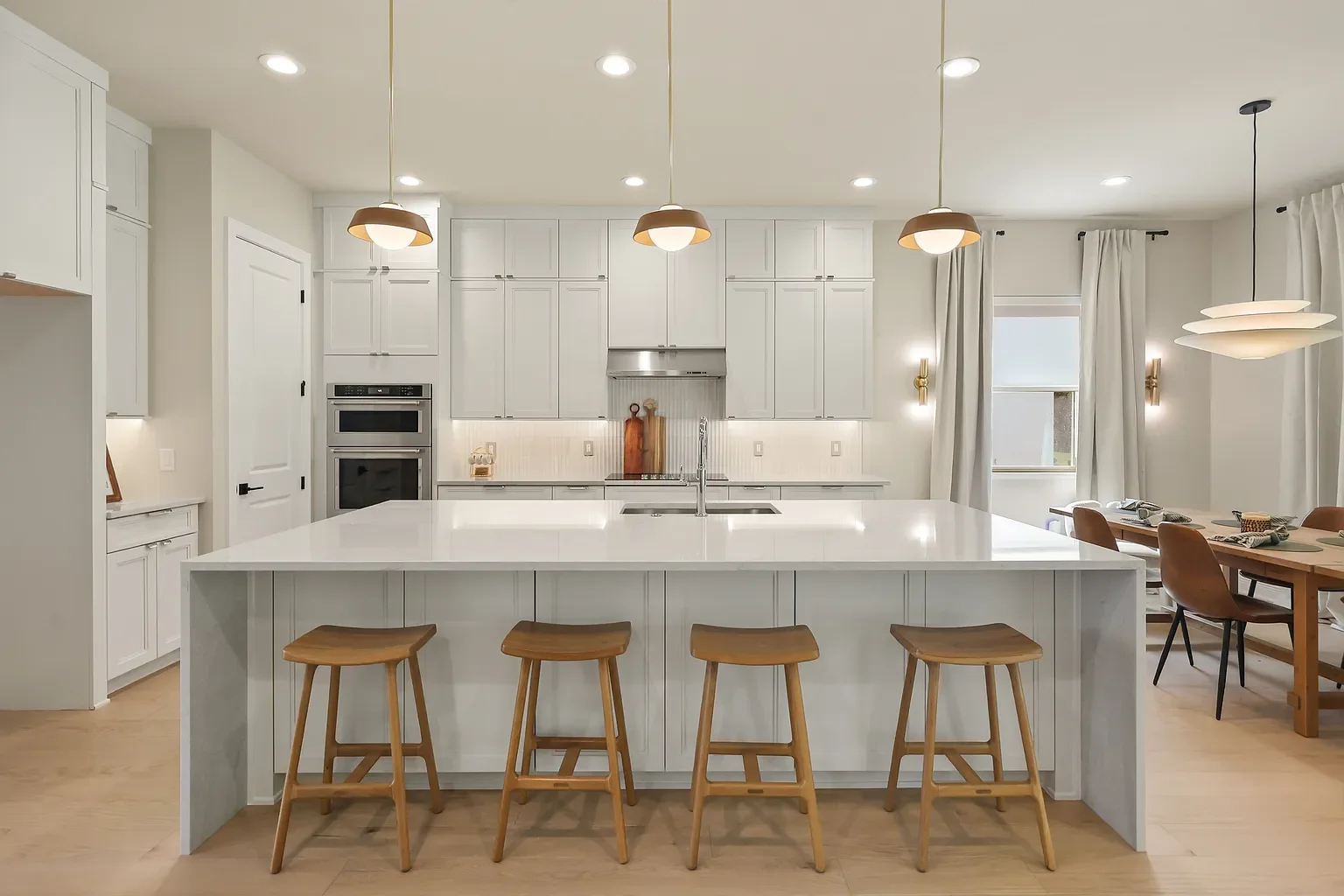 Modern kitchen with light wood cabinetry, white marble island, stainless steel refrigerator, open shelving, three pendant lights, and wood flooring