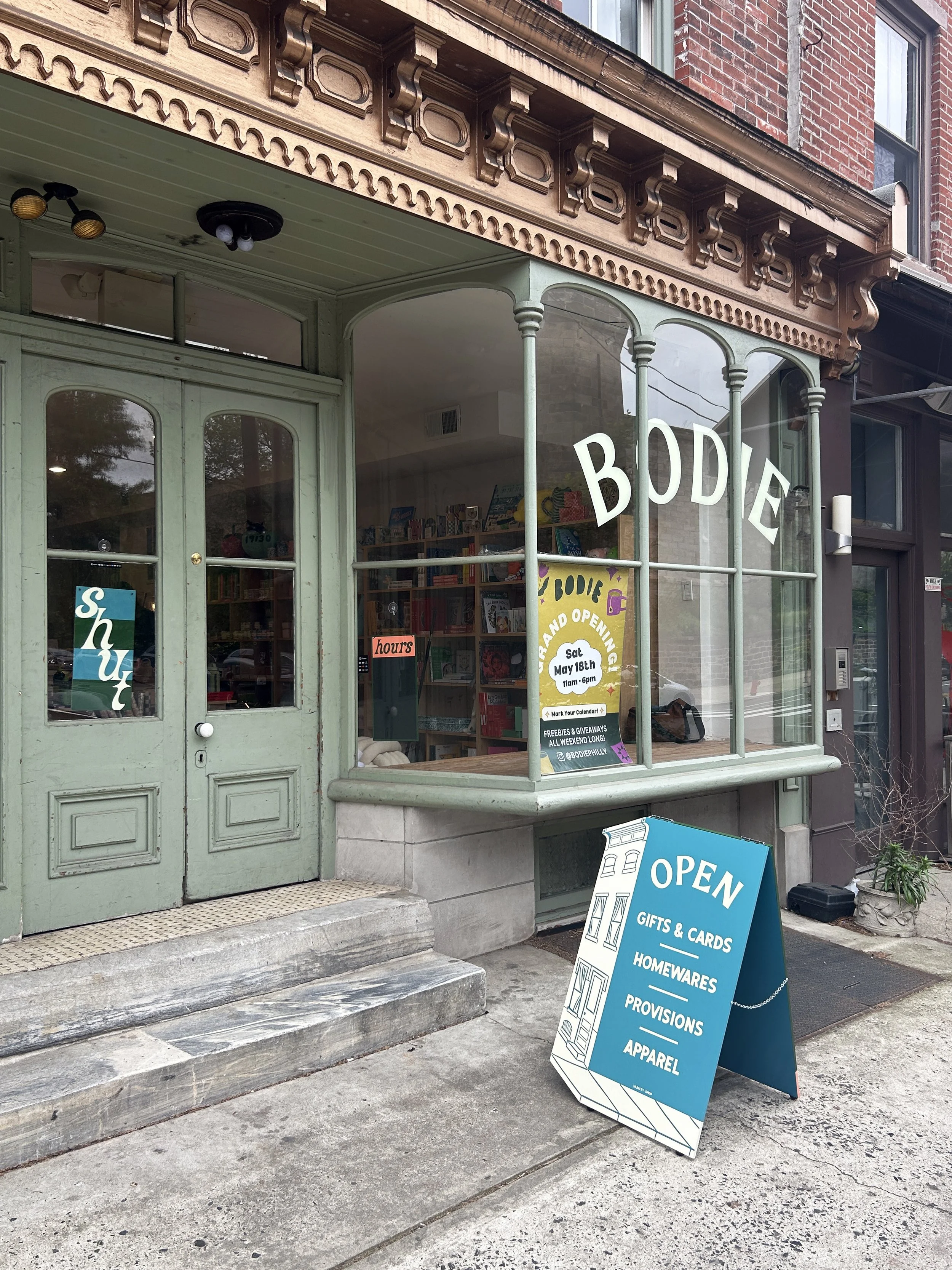 Bodie storefront with sandwich board, painted window and other small signs.