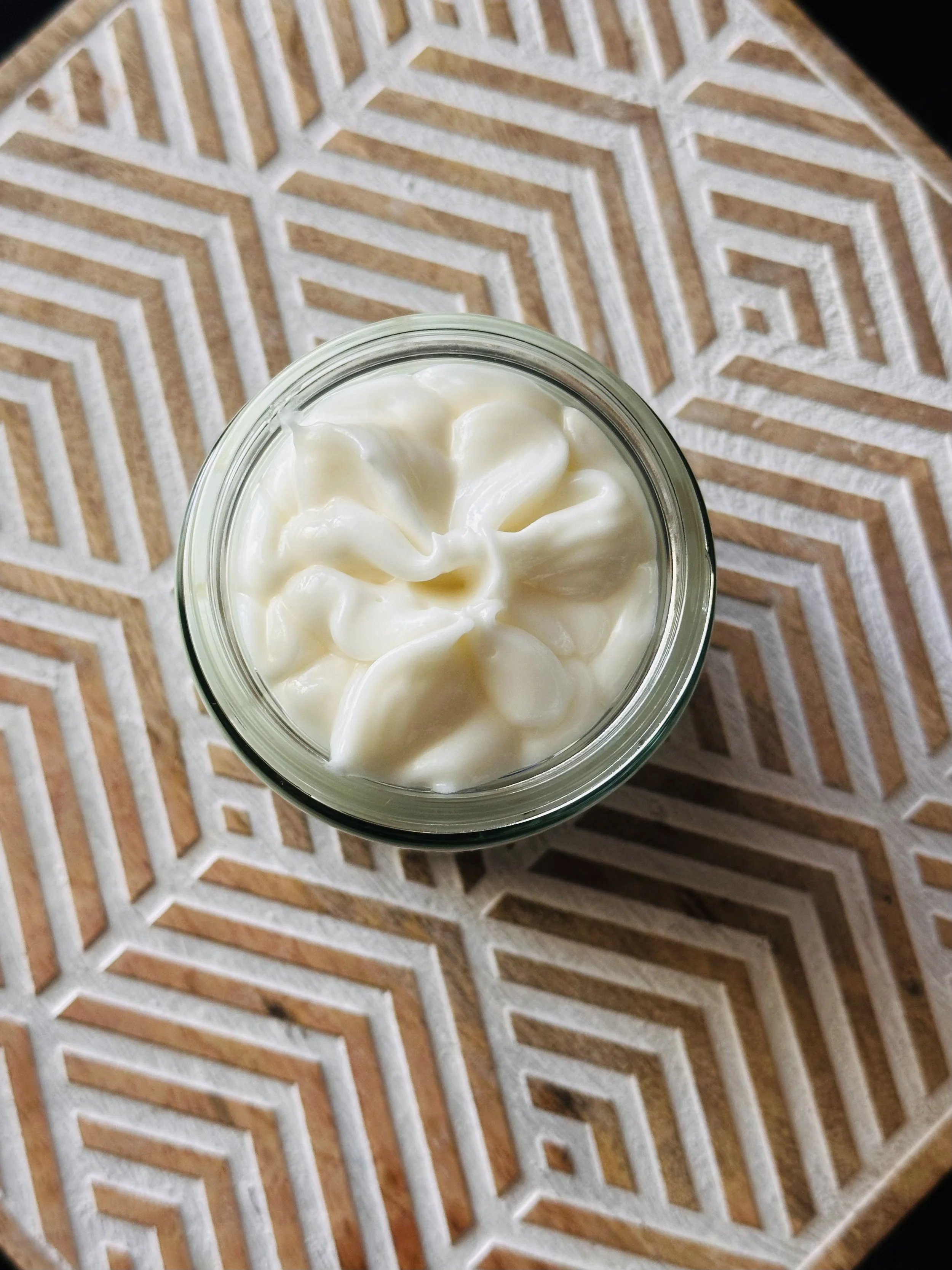A jar of mayonnaise or similar creamy condiment on a wooden surface with a geometric pattern.