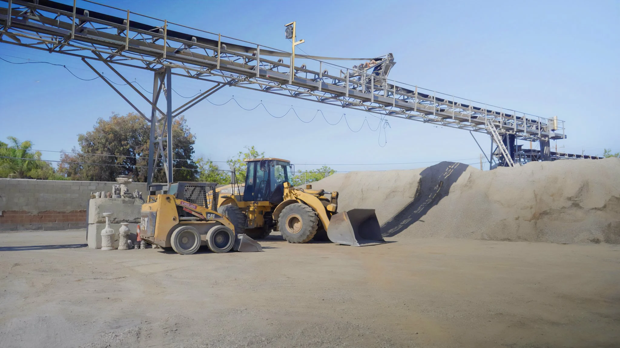 Construction site with a yellow bulldozer and a smaller loader under a scaffolding structure, with piles of dirt and concrete blocks nearby.