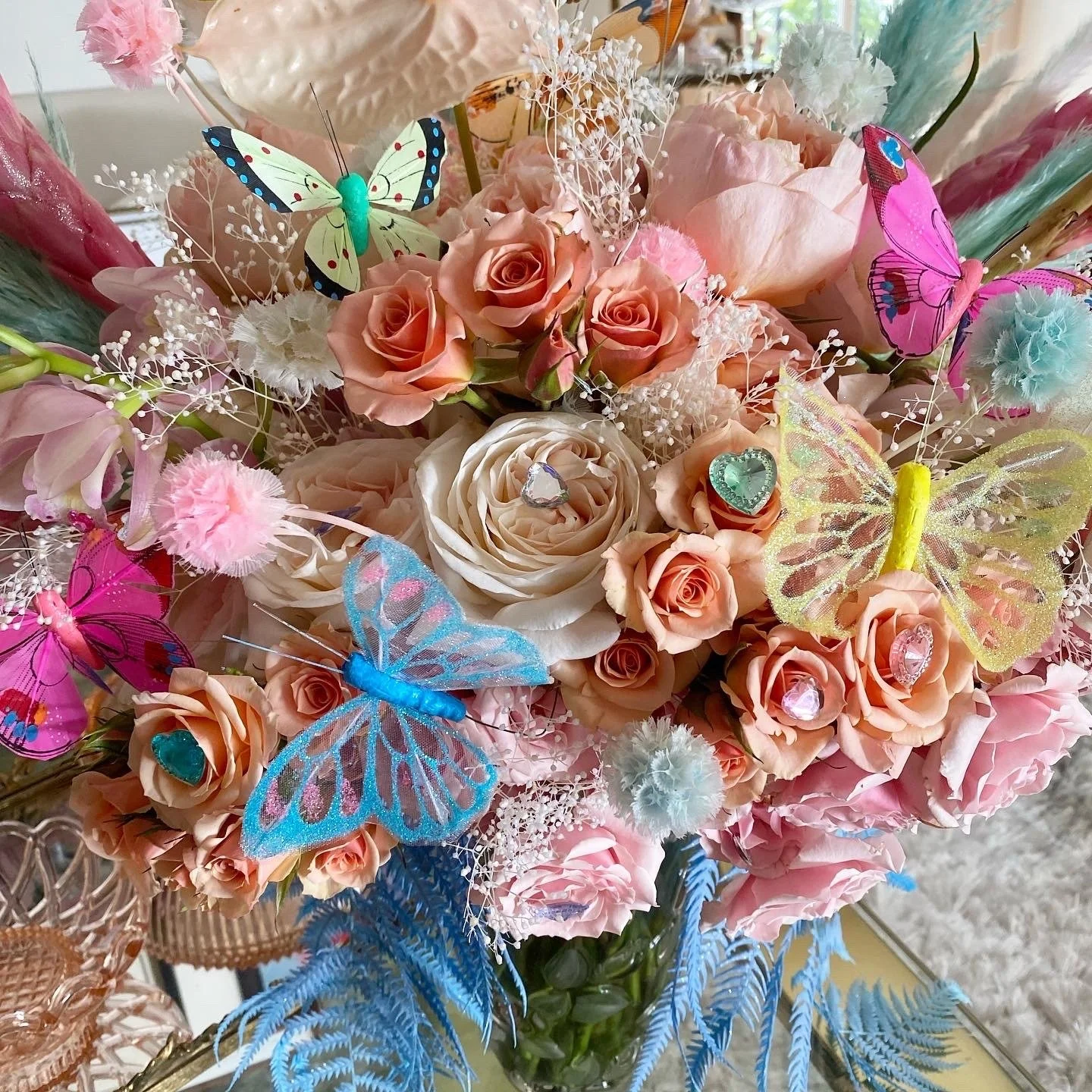 A bouquet of peach and pink roses, decorated with colorful artificial butterflies and small decorative hearts.