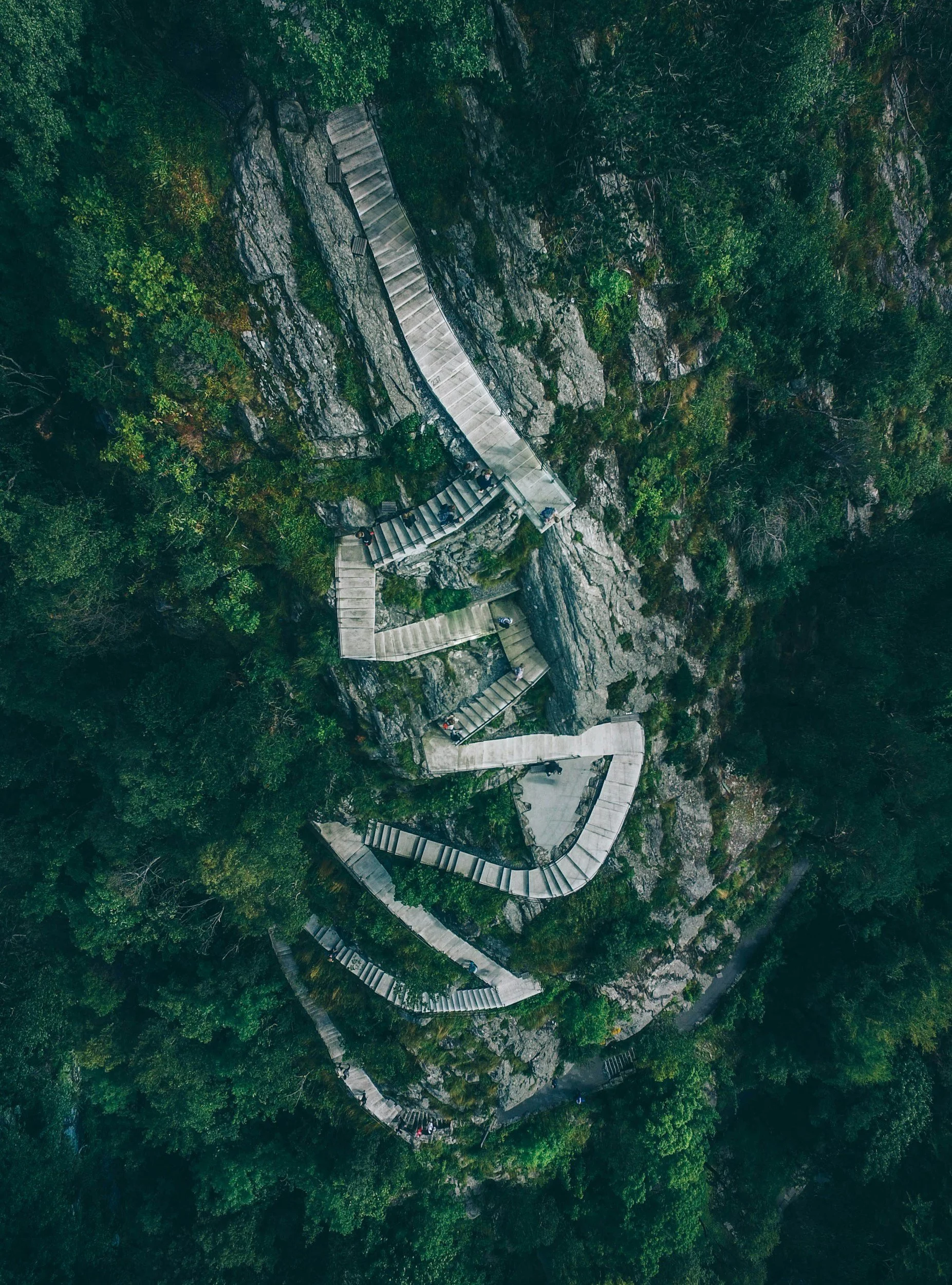 An aerial view of a winding staircase built into the side of a rocky, forested mountain.