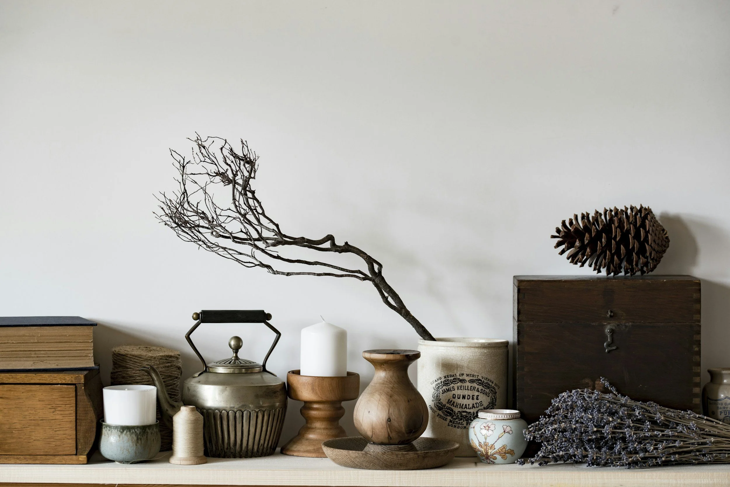 A variety of decorative vases and bowls of different shapes, sizes, and materials displayed on a shelf against a plain wall, with some wooden furniture and dried branches.