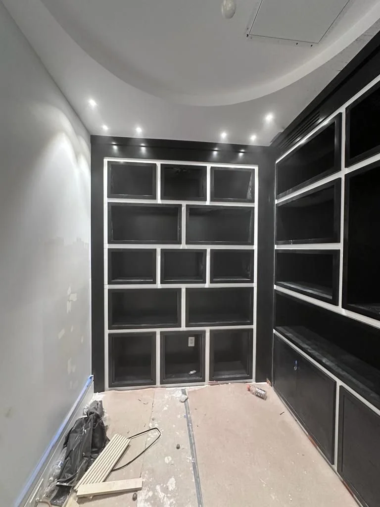 Empty black built-in shelving units in a room under construction with tools on the floor.