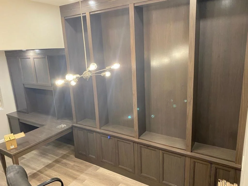 Empty dark wood built-in shelves and cabinets in a room, with a modern chandelier hanging overhead.