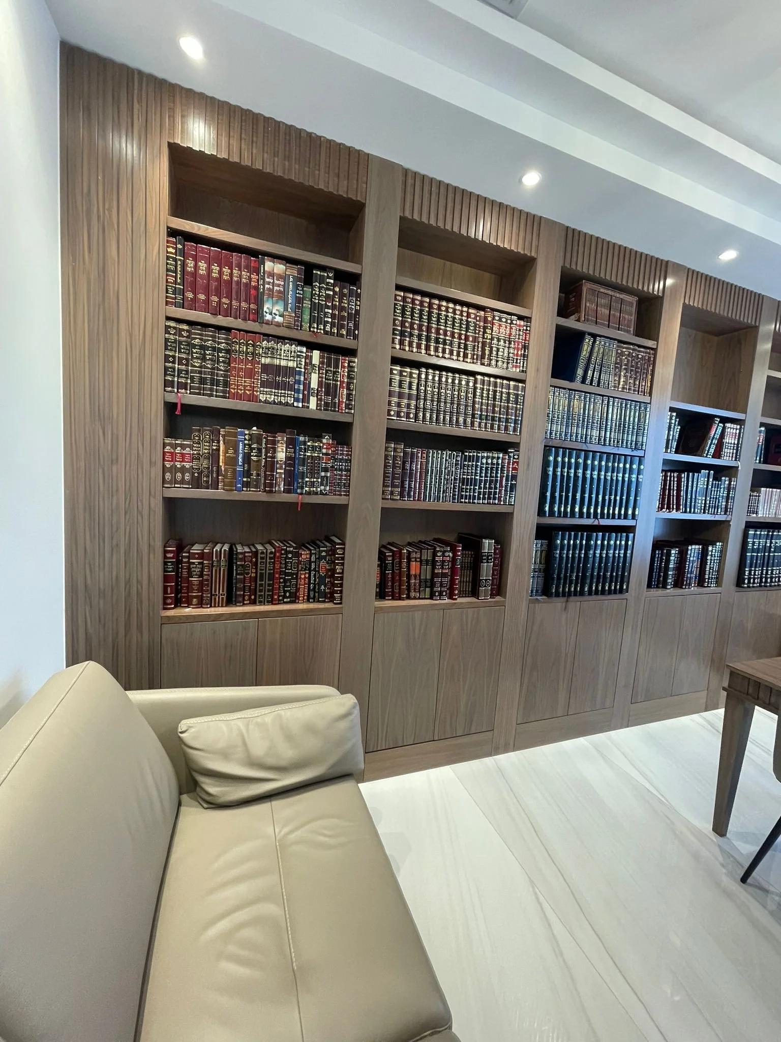 Library with wooden bookshelves filled with leather-bound books, cream sofa, and a light-colored floor.