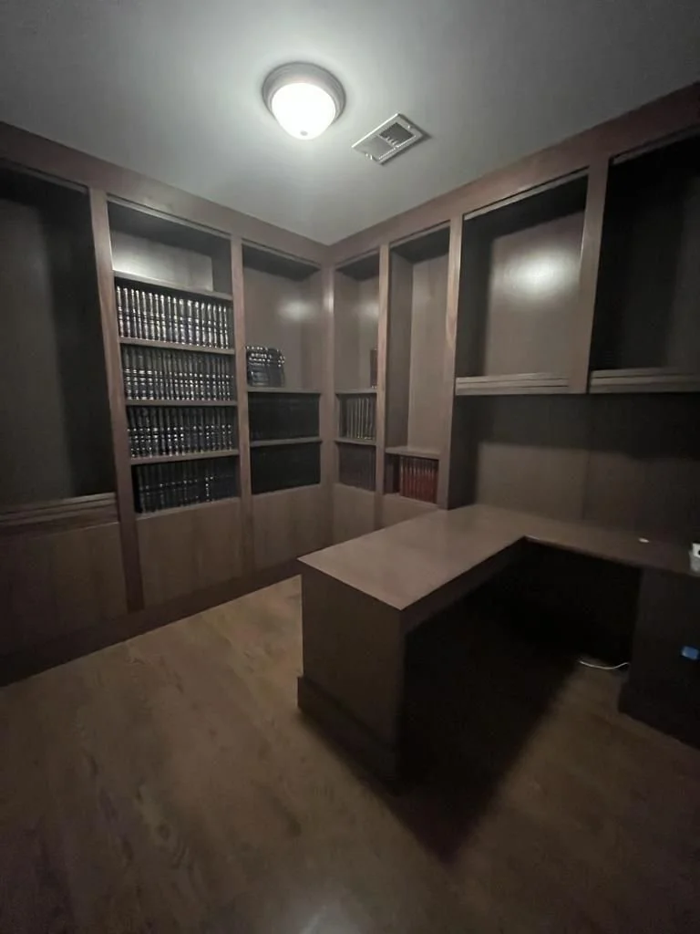 Empty home office with wooden bookshelves filled with books, a wooden desk, and a ceiling light fixture.